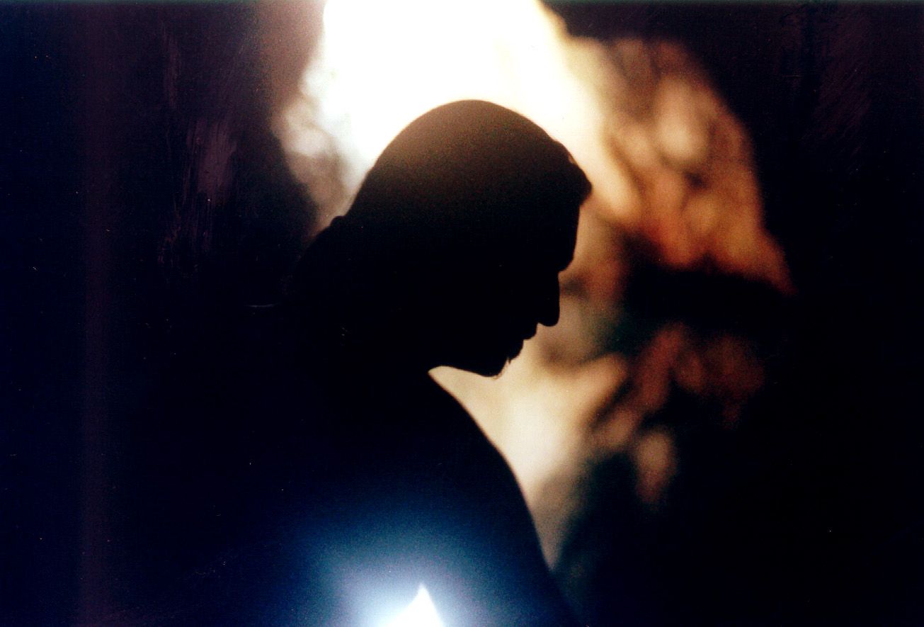 A dark silhouette of a person in profile with warm glowing light and autumn foliage in the background.