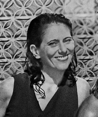 A black and white photo of a smiling woman with wet dark hair in front of a patterned background.