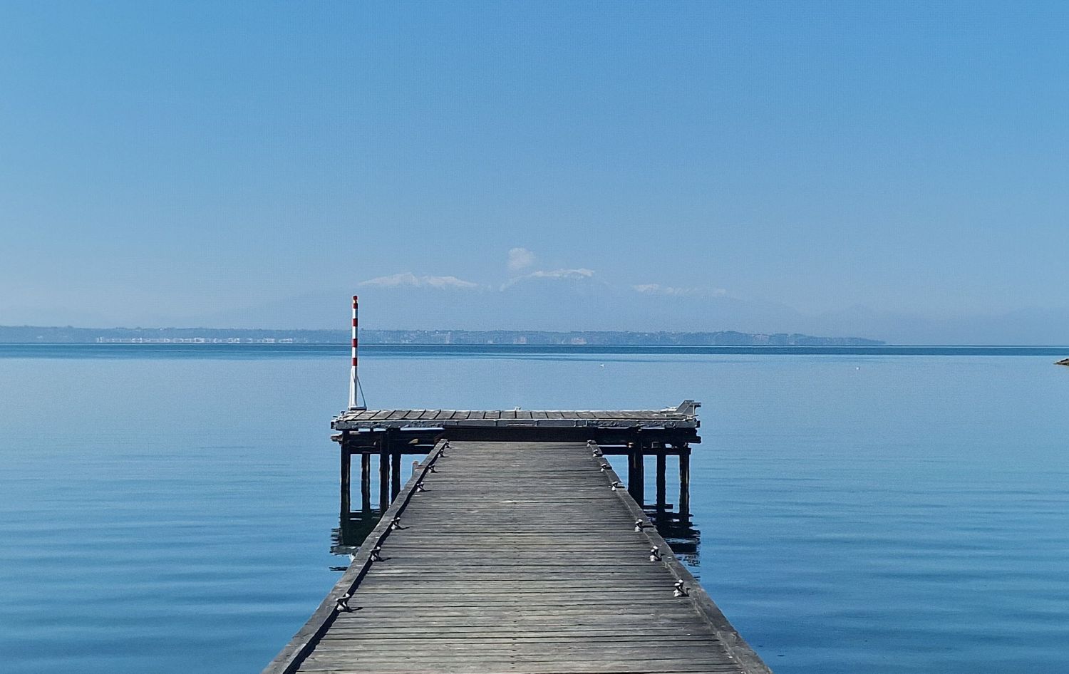 Serene wooden pier extending into calm blue lake water under clear sky.