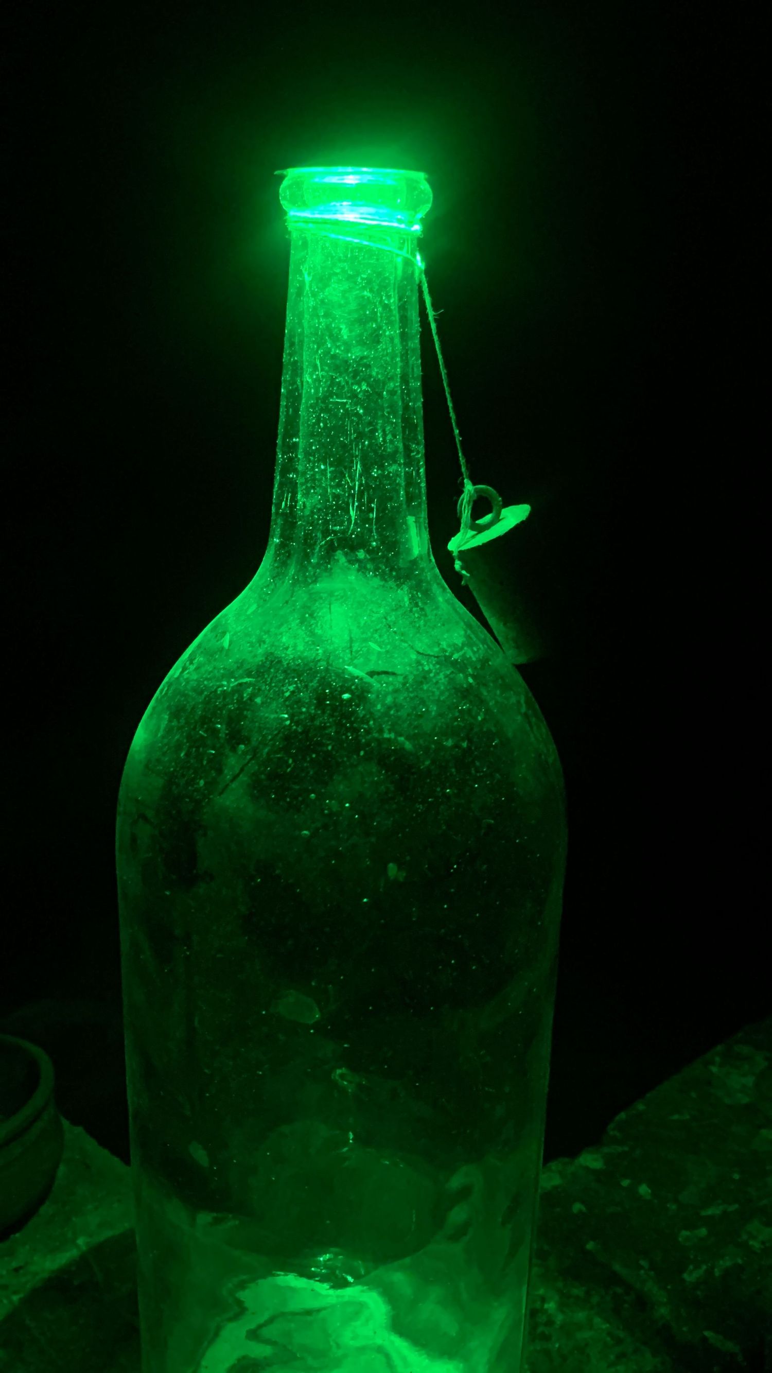 A glowing green antique glass bottle illuminated against a dark black background.