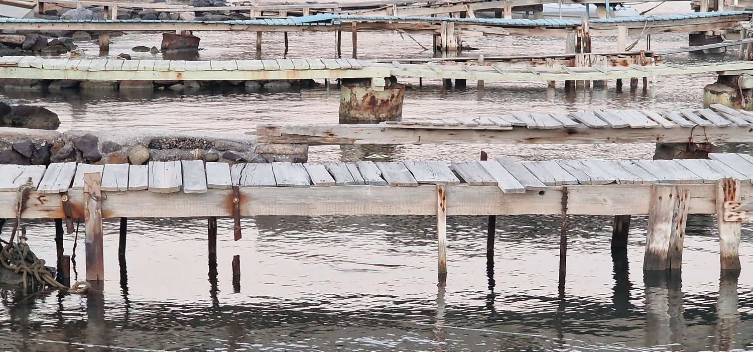 Weathered wooden dock structures standing in shallow coastal water, showing signs of age.