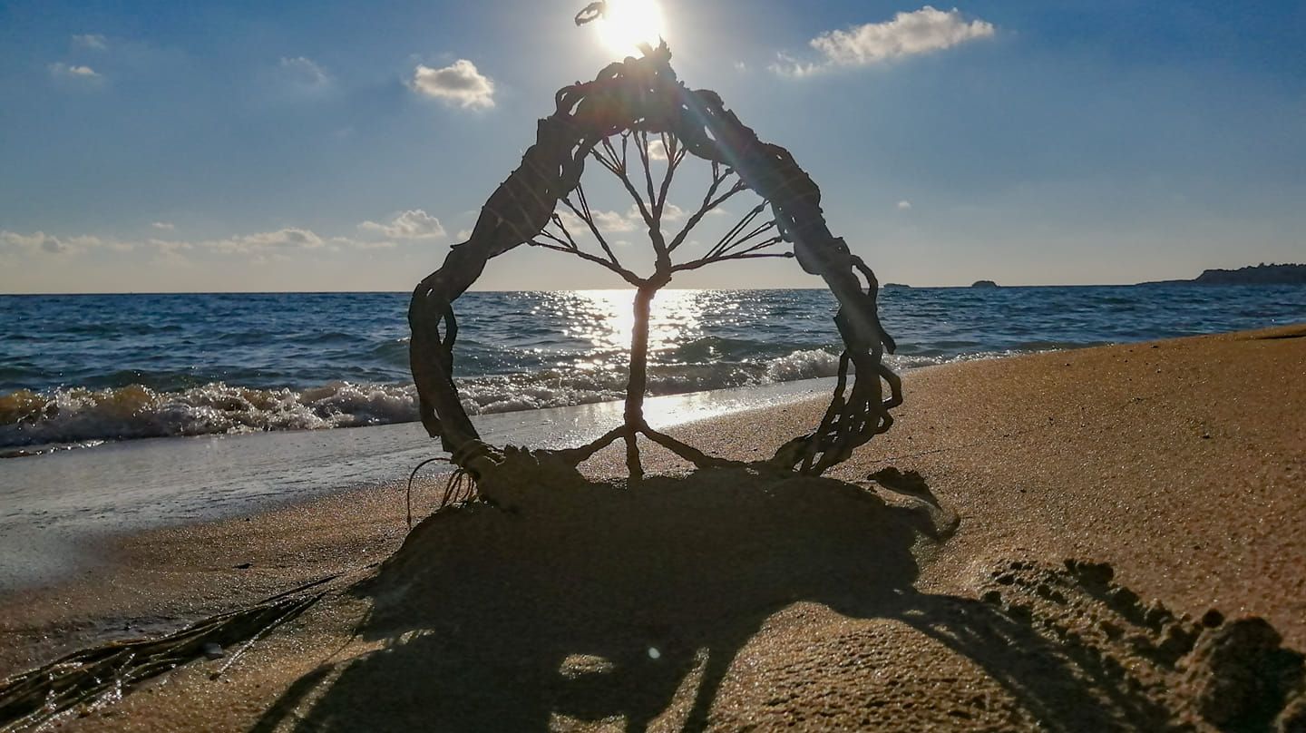Decorative tree sculpture framing ocean sunset on sandy beach at golden hour.