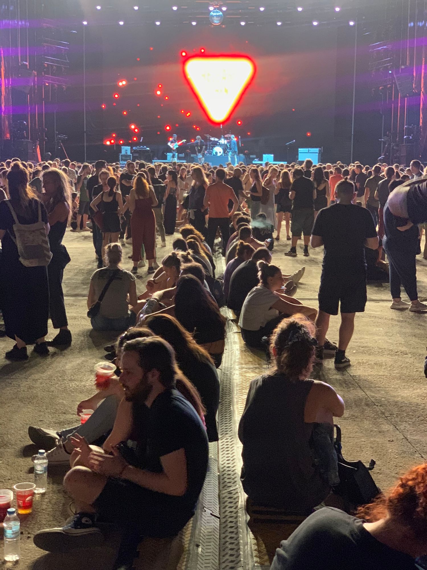 Large outdoor music festival crowd gathered before a lit stage with a glowing triangle logo at night.