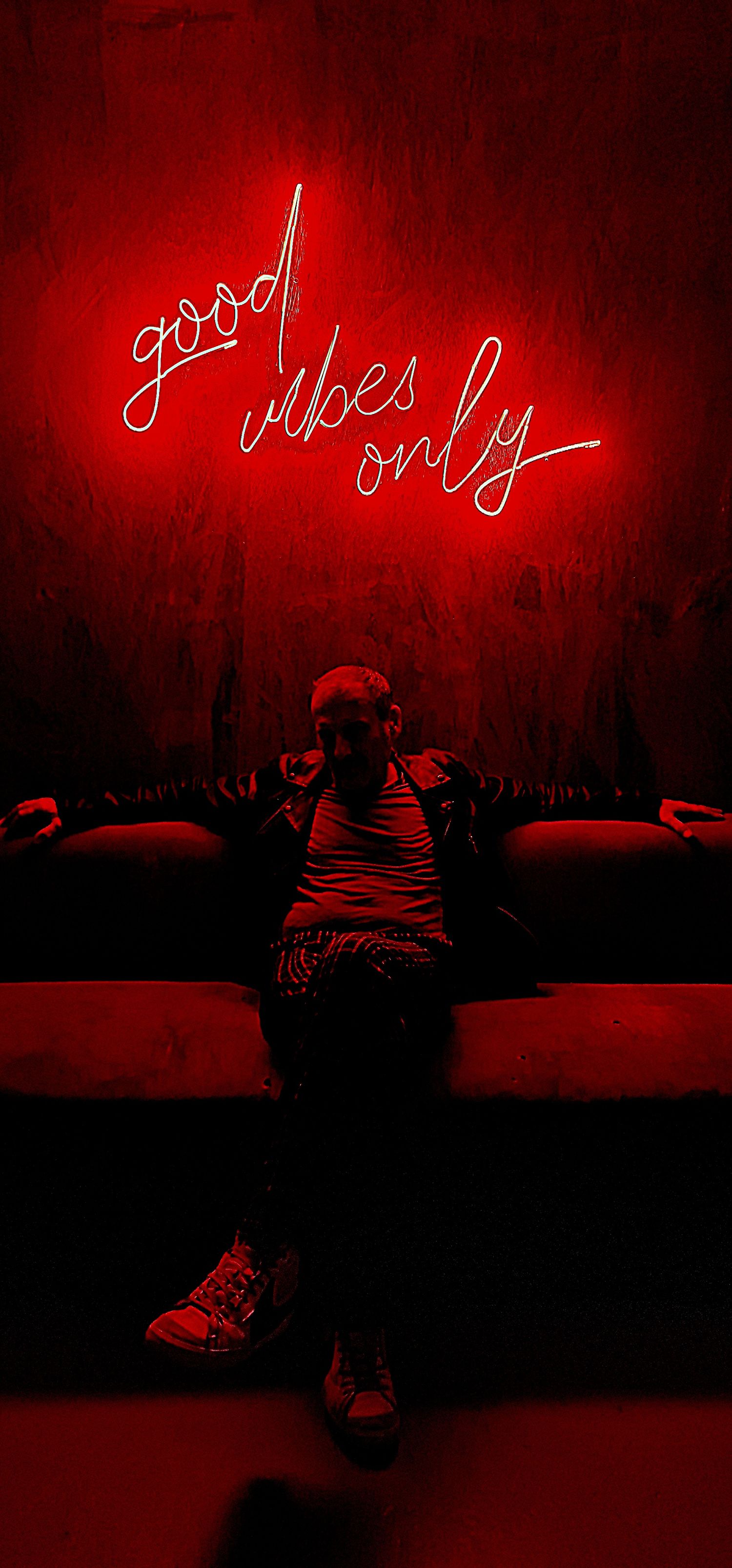 Person sitting under a red neon sign reading good vibes only in a dimly lit red room.
