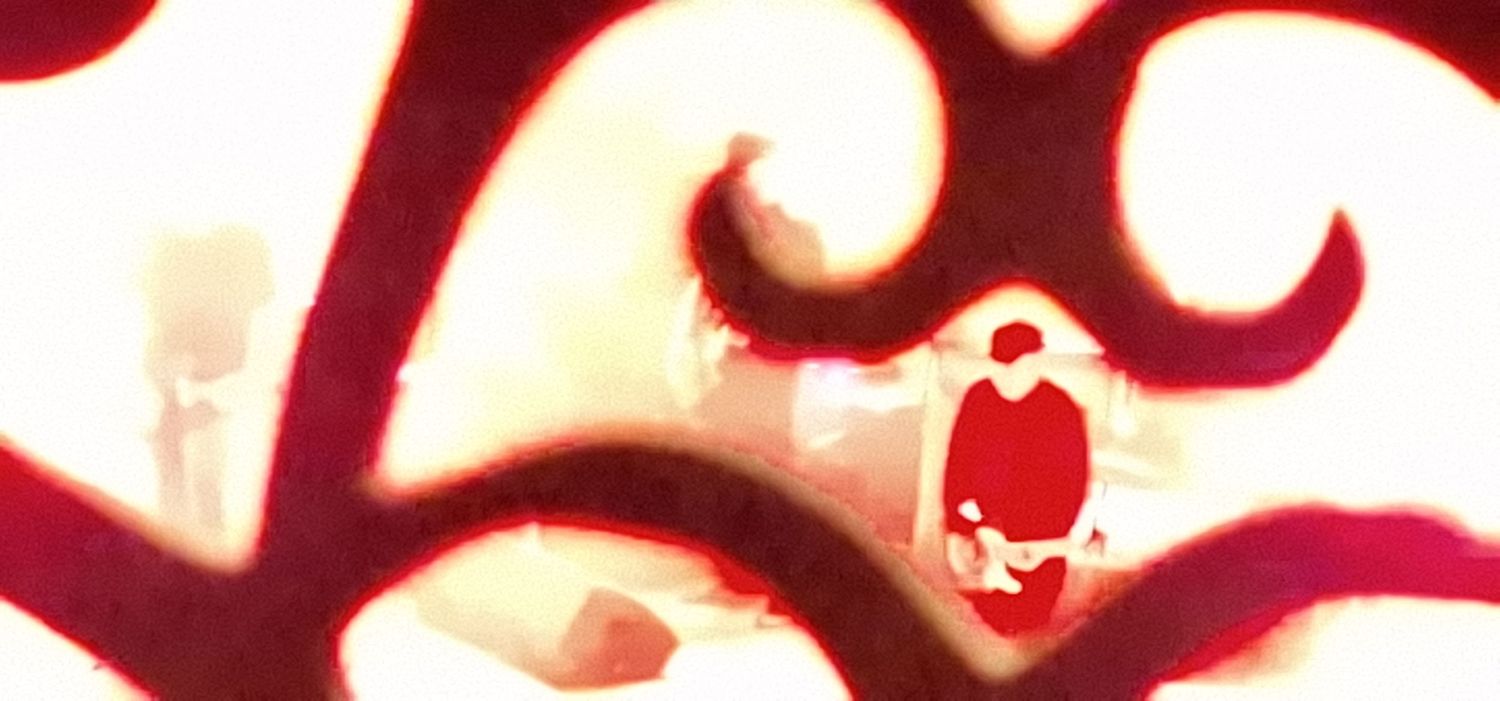 A dramatic red and white artistic image of a figure seen through ornate swirling patterns.