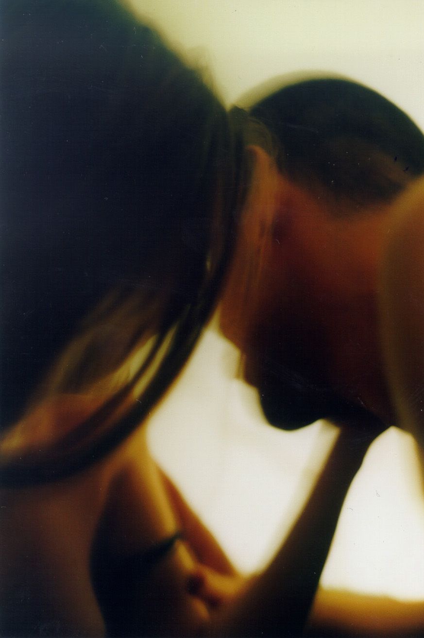An artistic blurred close-up portrait of two people leaning toward each other in warm tones.