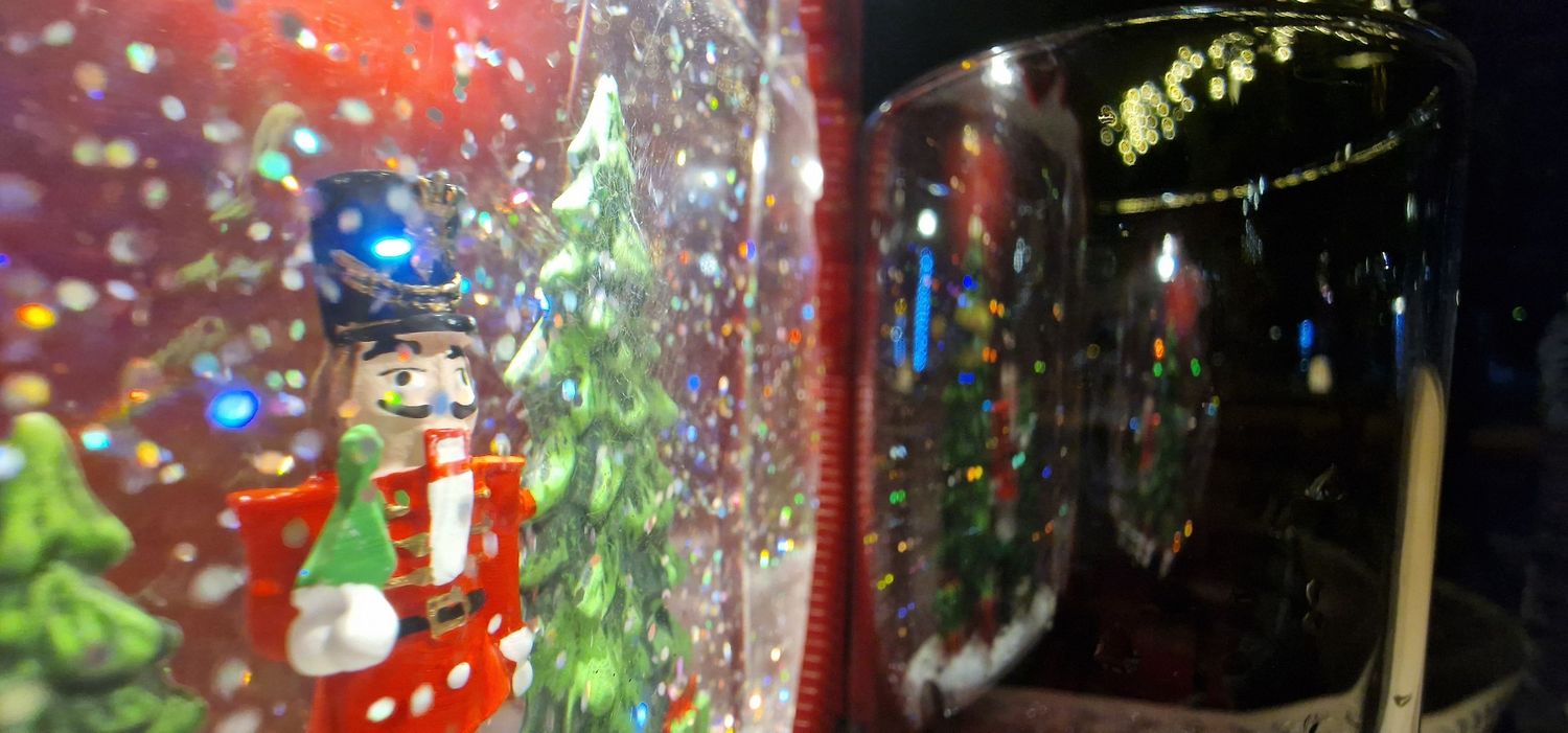 Close-up of colorful Christmas snow globes with nutcracker and snowman figurines surrounded by glitter.