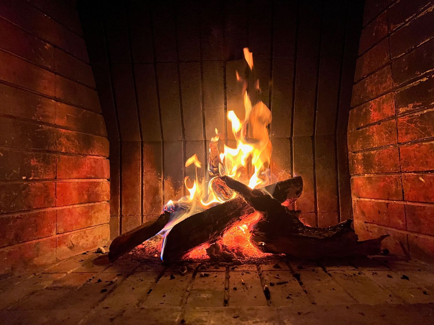 Warm glowing fire burning with logs in a classic red brick fireplace.