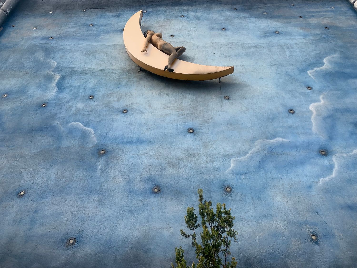 Artistic building mural featuring a crescent moon sculpture against a painted blue sky.