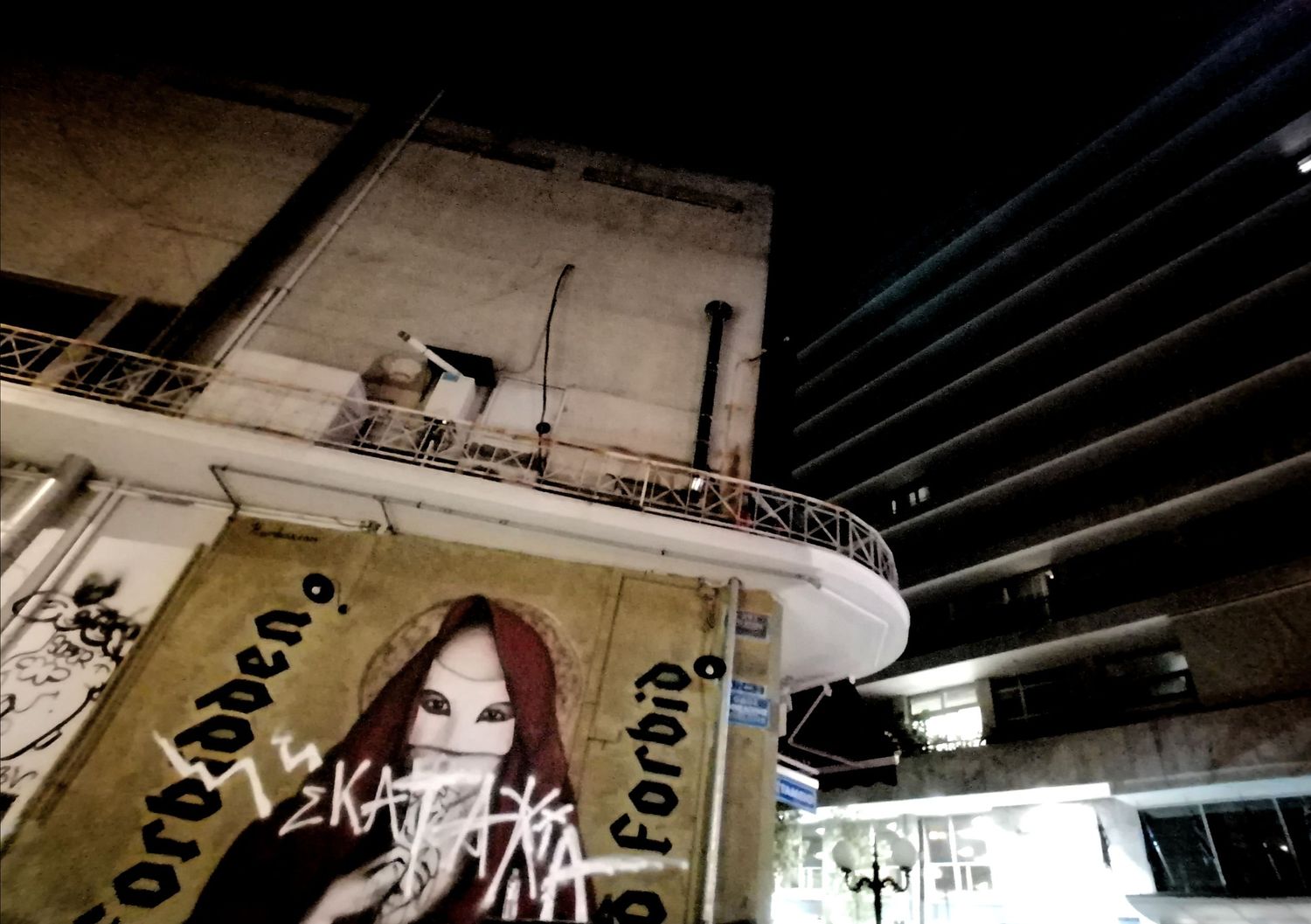 Night urban scene with graffiti-covered wall featuring a woman's portrait beneath an elevated structure.