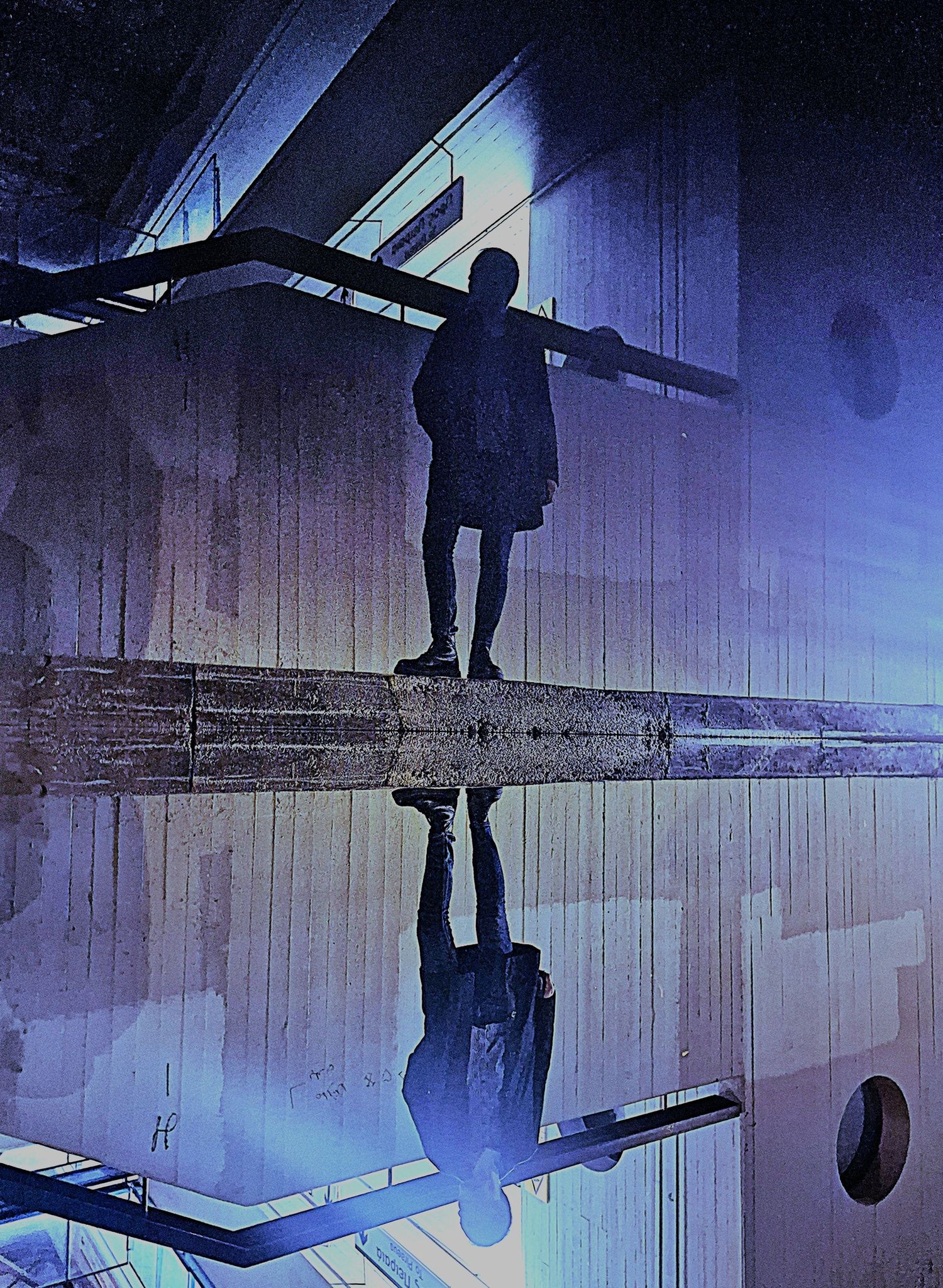Silhouette of a person standing on a ledge reflected in water with dramatic blue urban lighting.