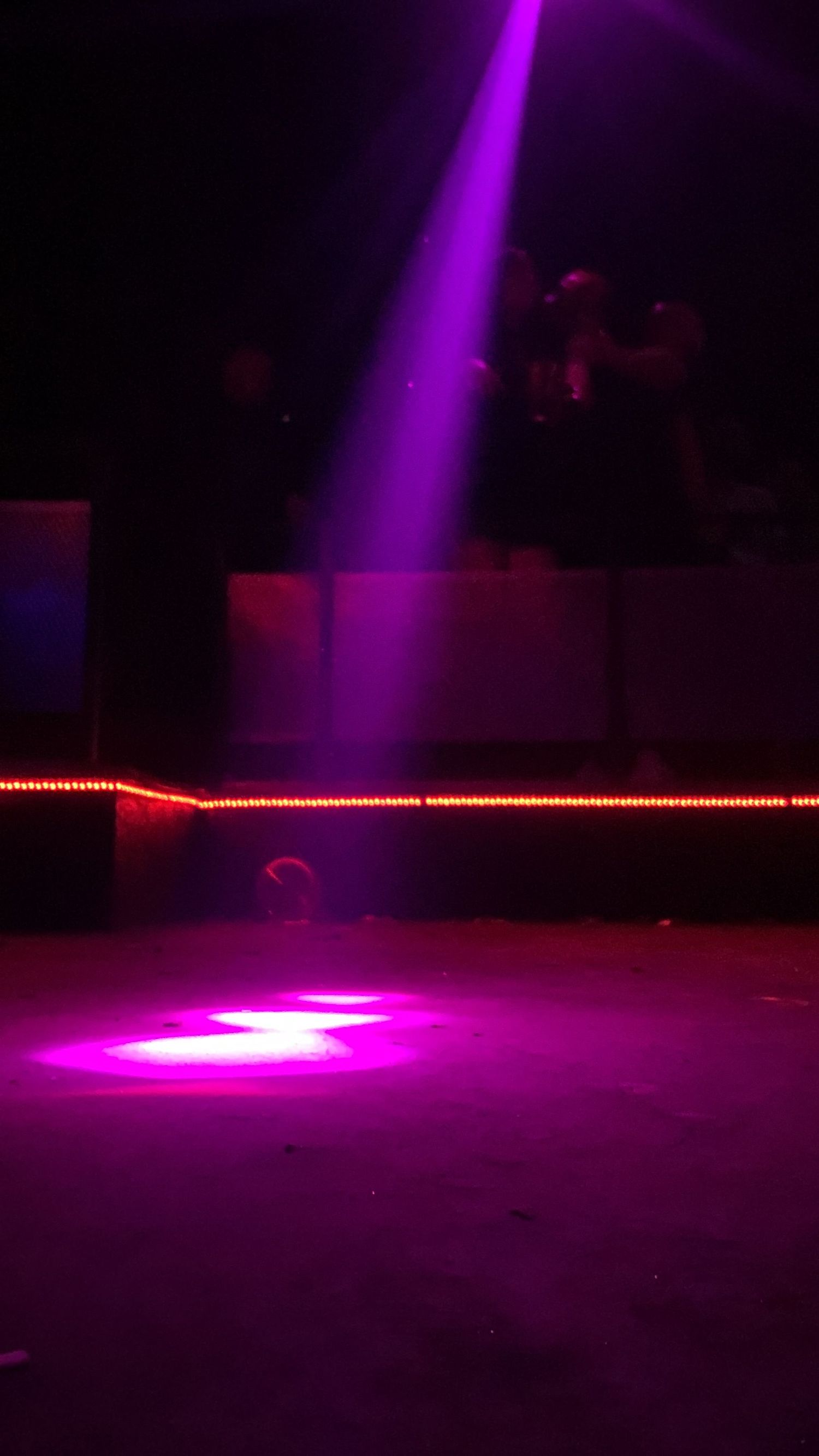 Dark nightclub interior with dramatic purple and pink stage lighting beams.