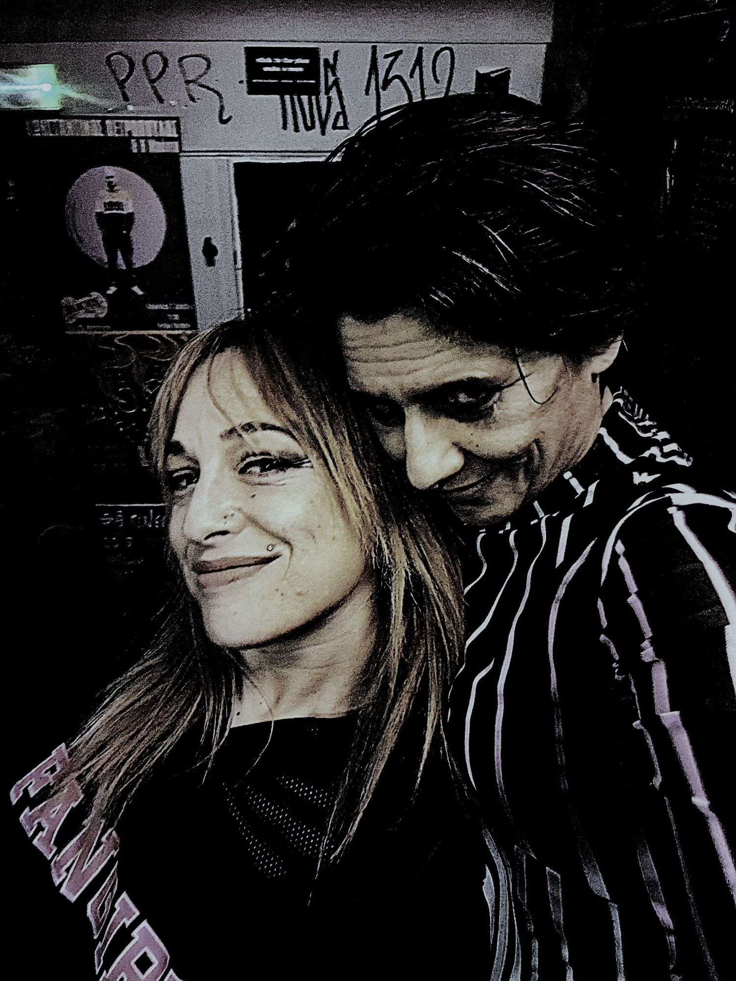 High-contrast edited photo of a smiling woman and a man with face paint in a dark setting.