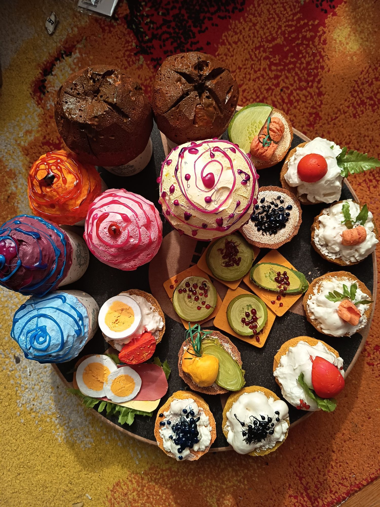 An elegant overhead view of a colorful assortment of decorated open-faced sandwiches and cupcakes.