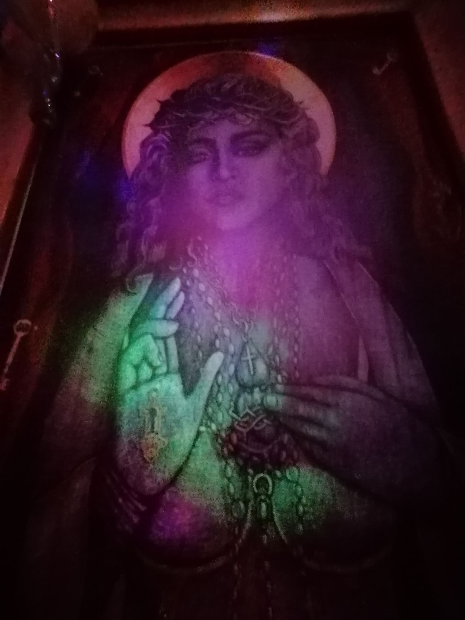 Glowing religious icon painting of a saint with halo under colorful UV blacklight illumination.