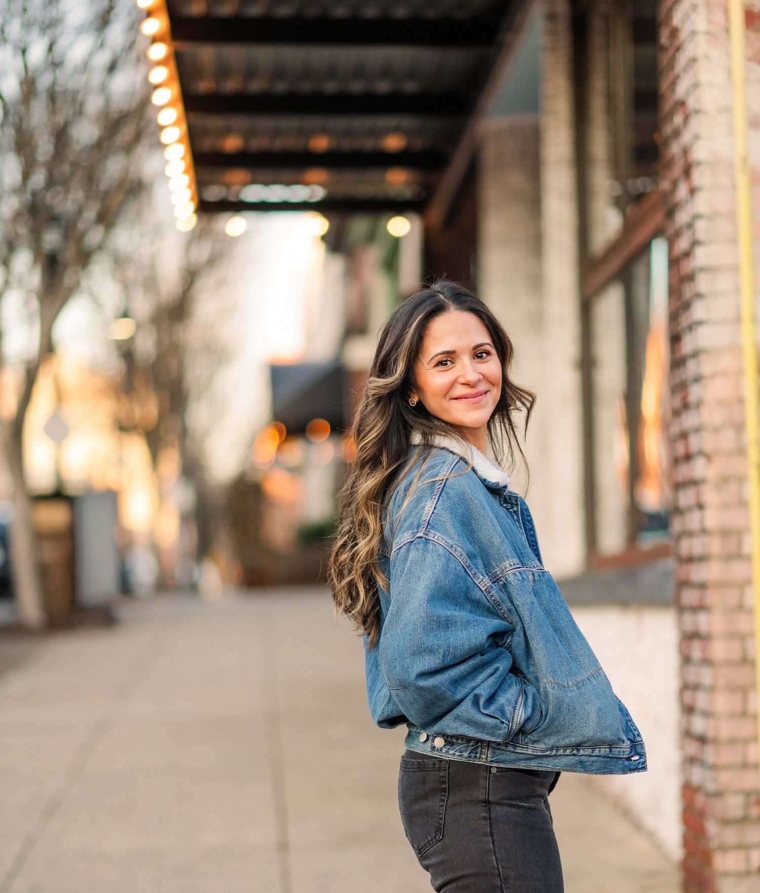 A casual portrait in an urban setting with string lights and brick walls in the background.