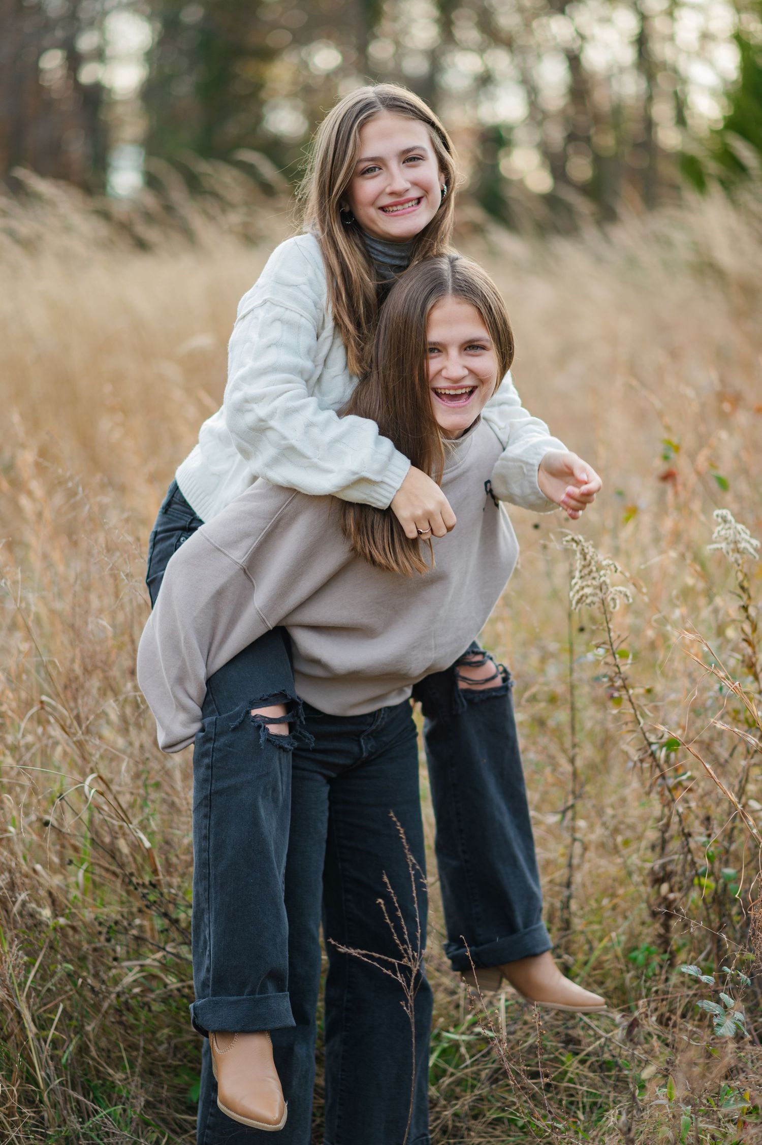 Two people in casual outfits share a playful piggyback ride moment in a tall grass field.