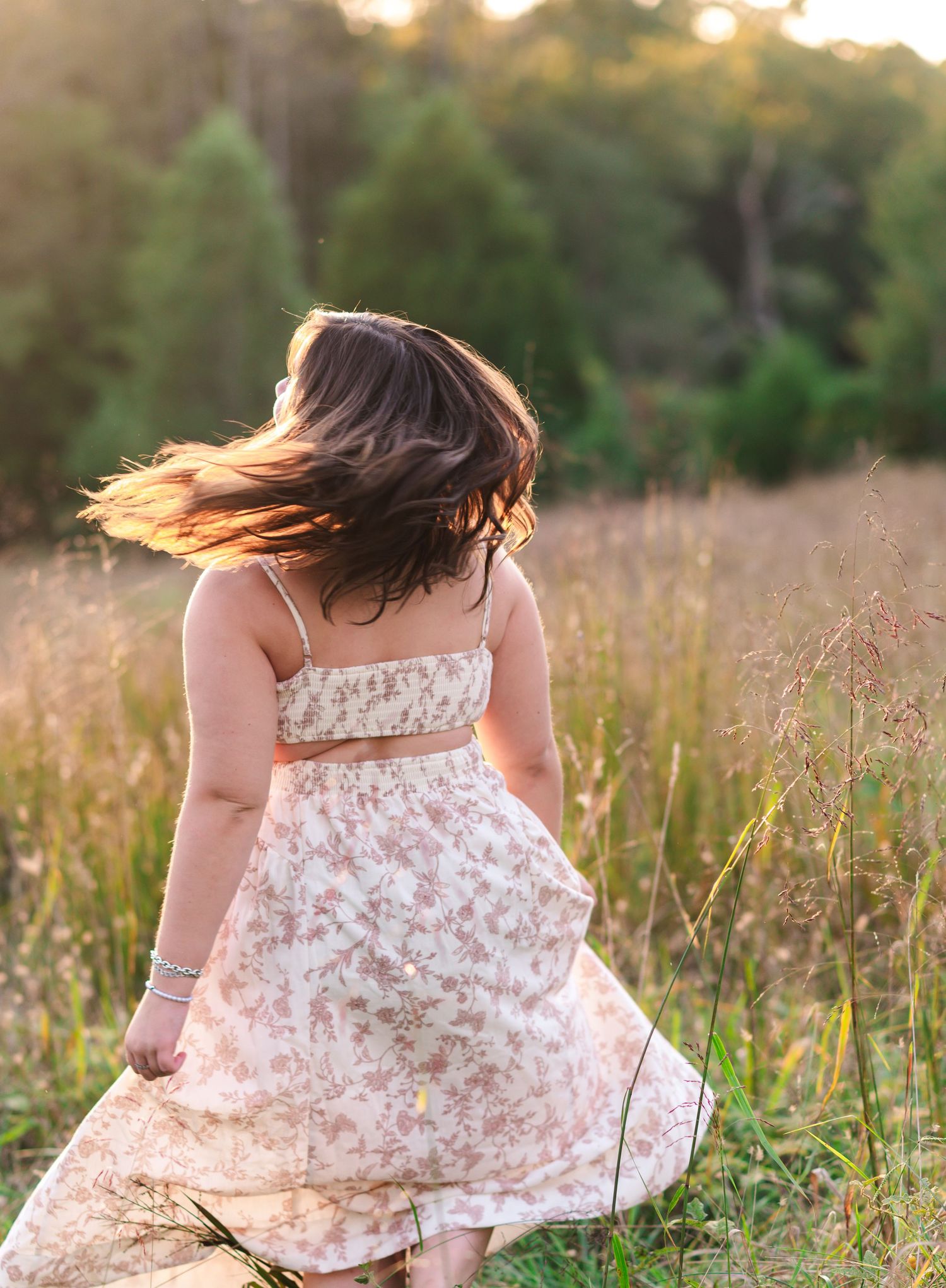 Person in floral dress twirling in a sunlit meadow with hair flowing in the wind.