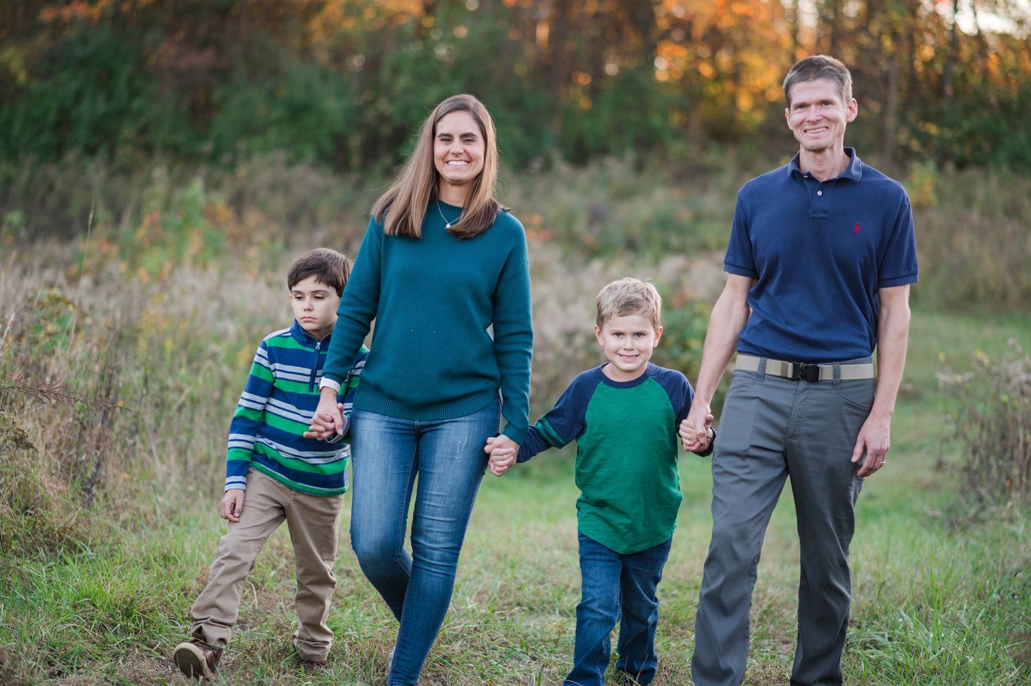 Family walking together through autumn field during golden hour portrait session.