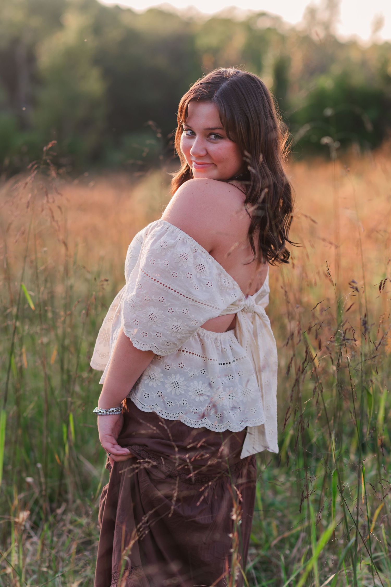 Portrait in field showing off-shoulder white lace top and brown skirt in golden hour lighting.