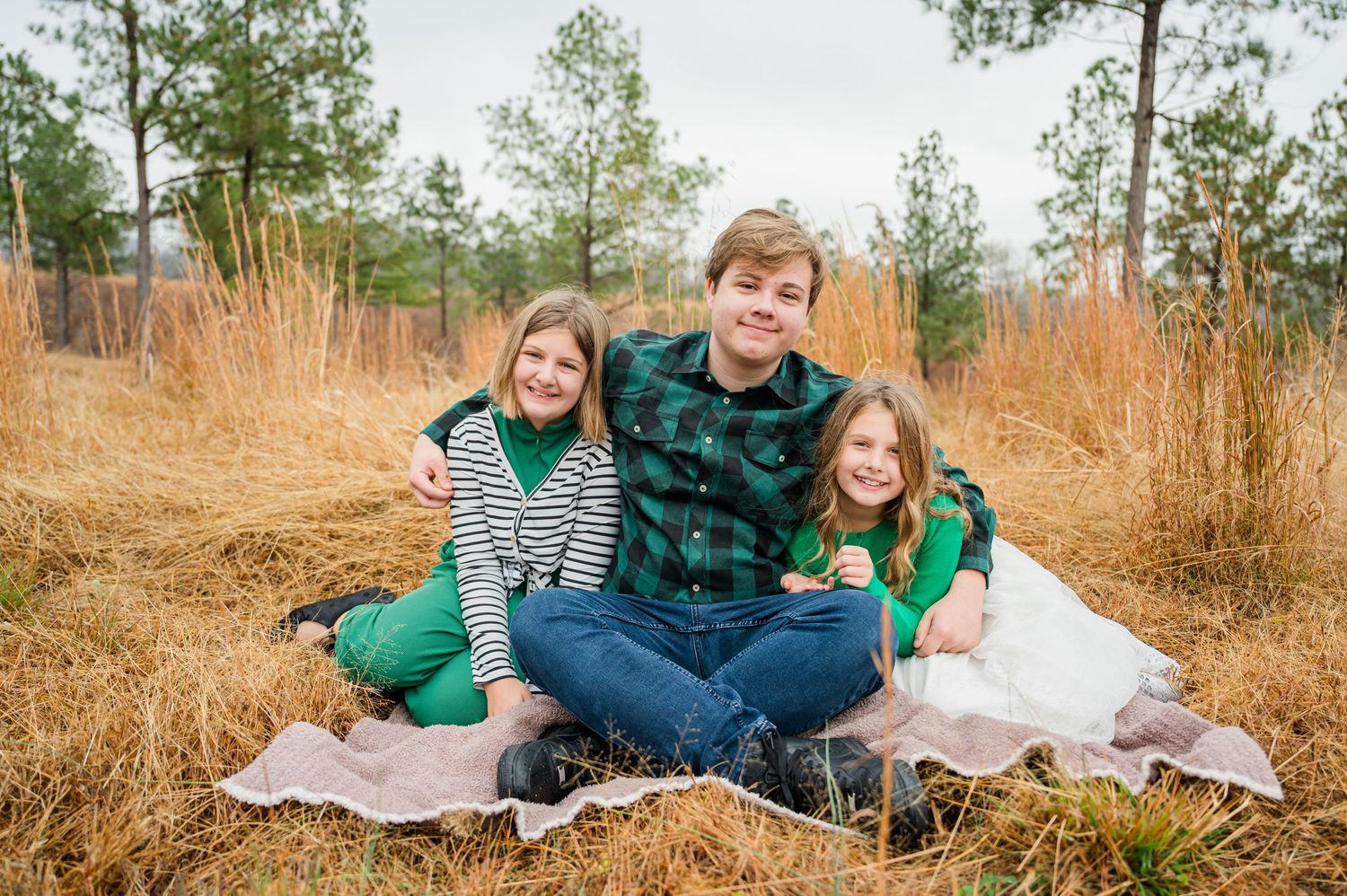 Family members relax together on blankets spread out in a pine forest setting.