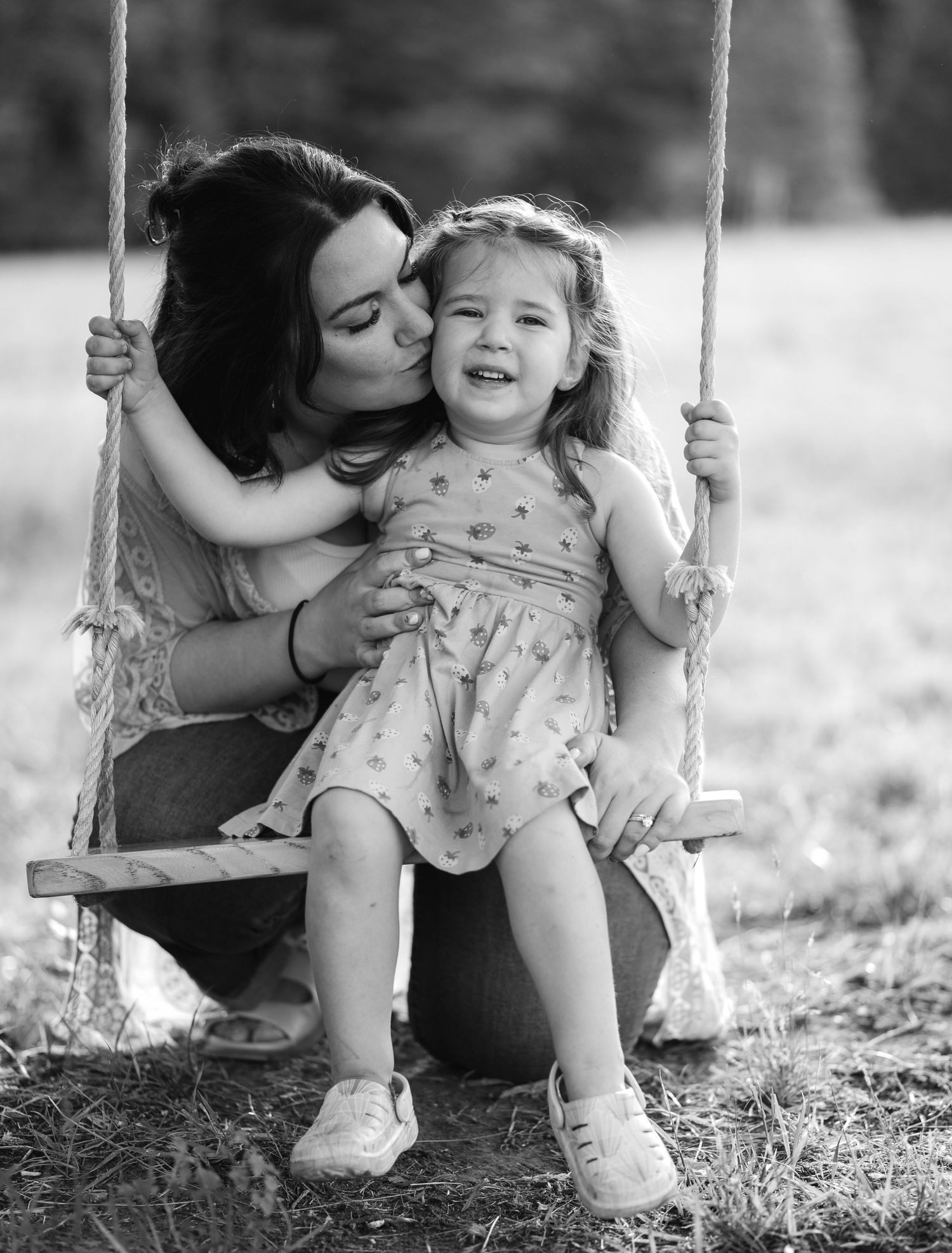 A tender black and white photo series showing loving moments between parent and child on a wooden swing outdoors.