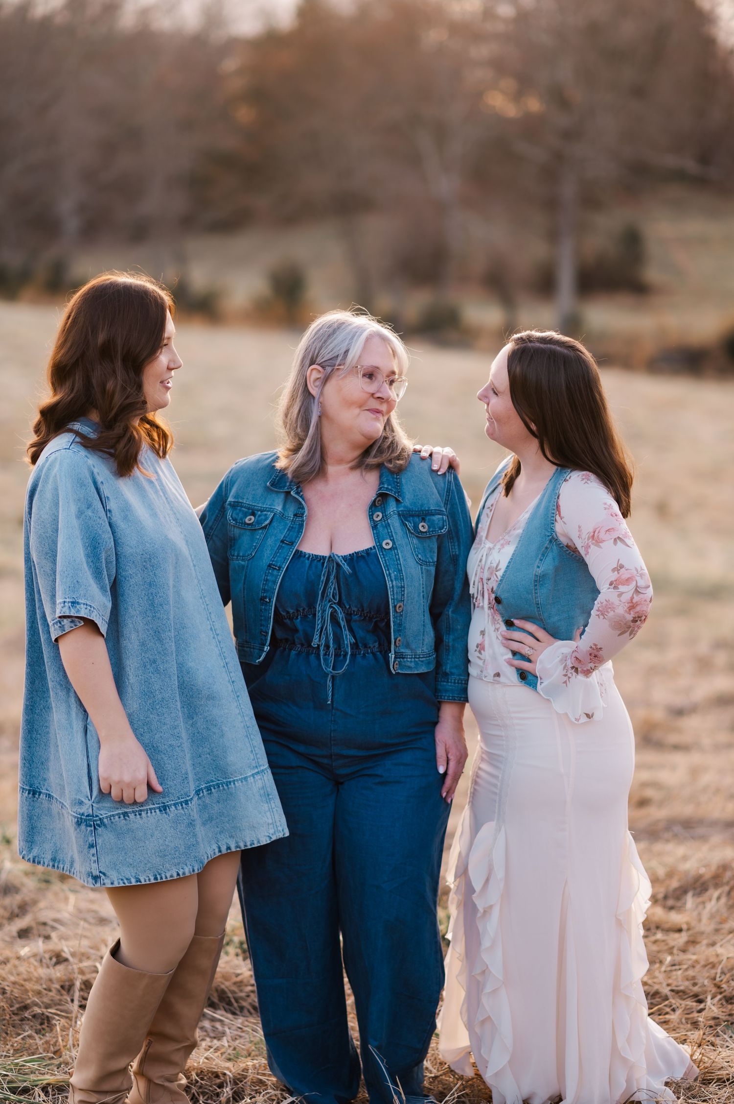 Three women in denim and casual wear share a joyful conversation together in a golden sunset field.