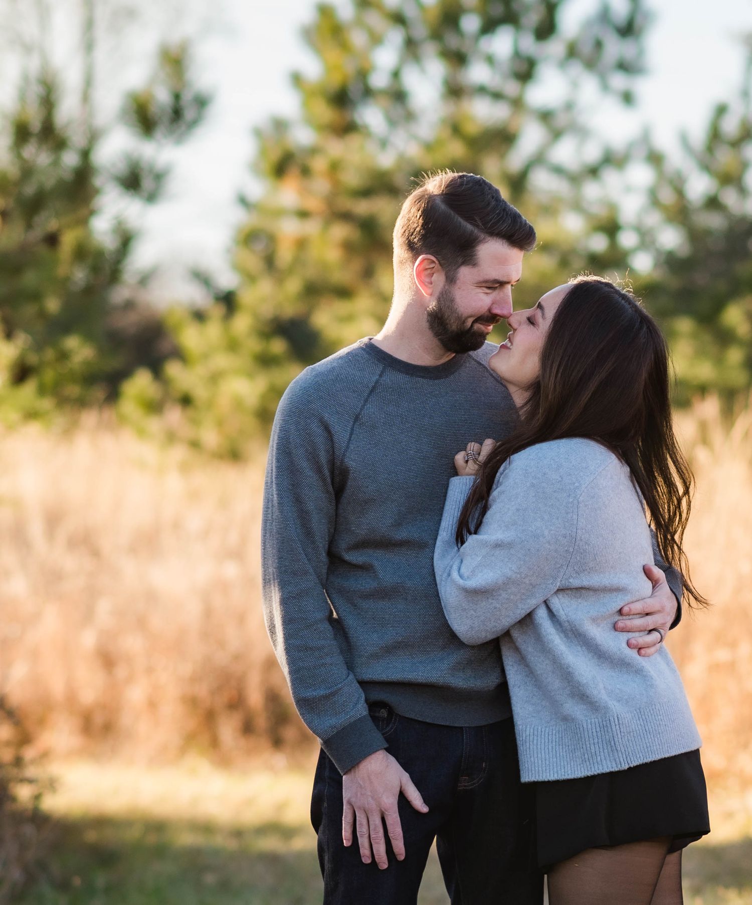 Couple in casual sweaters shares tender moments in a golden field at sunset.