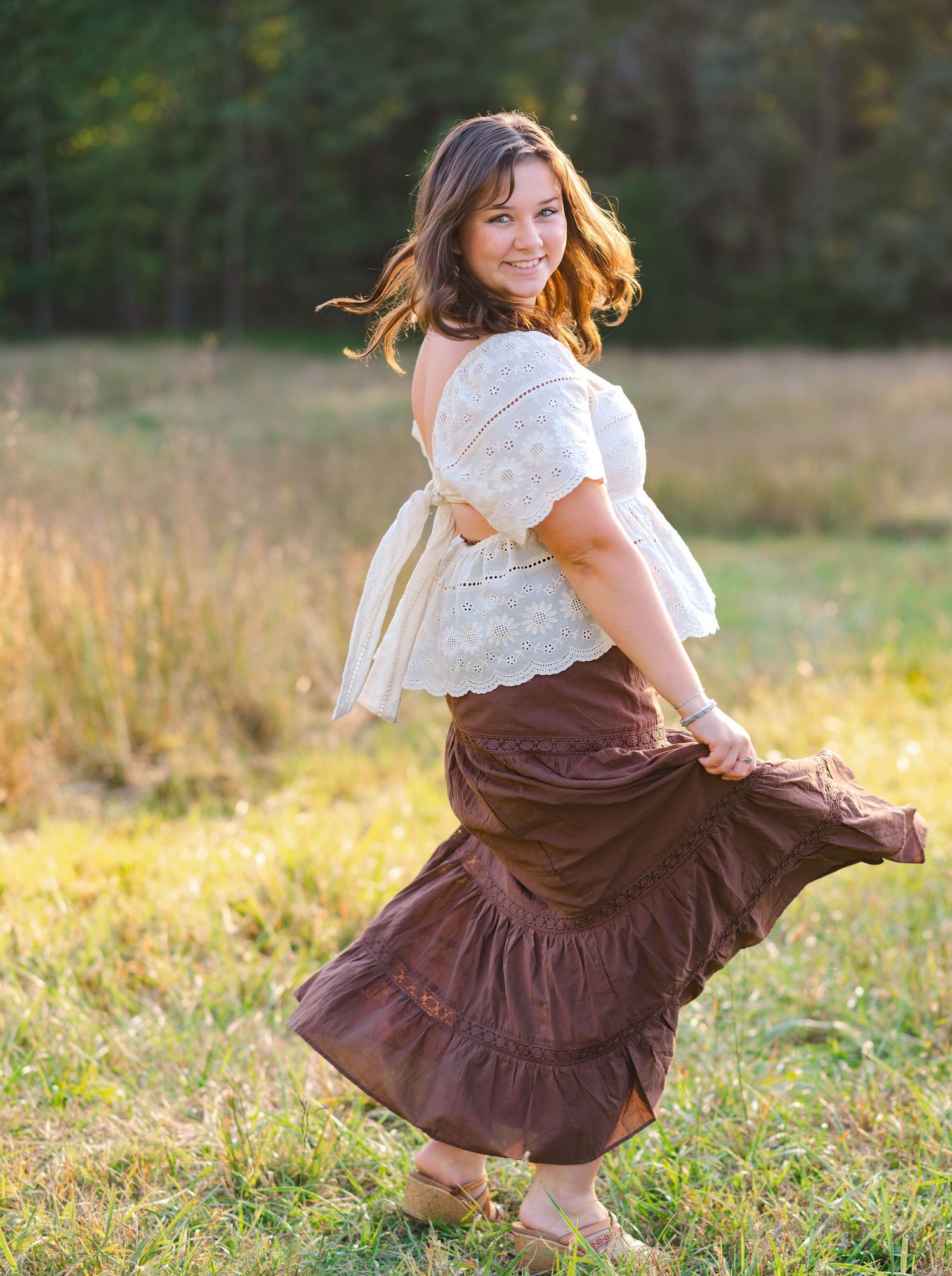 A child spins playfully in a brown ruffle skirt and white top in a golden field at sunset.