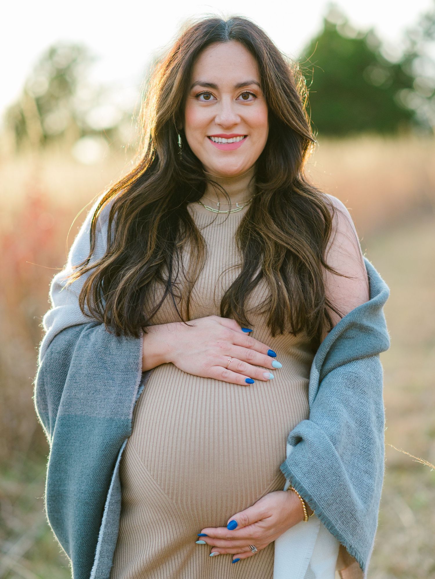 Maternity photoshoot in a field during golden hour featuring a woman in beige sweater and gray cardigan.