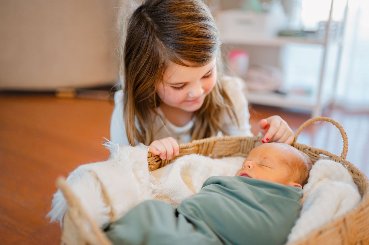 A baby lies on a white blanket while being gently touched by someone wearing a white sweater.