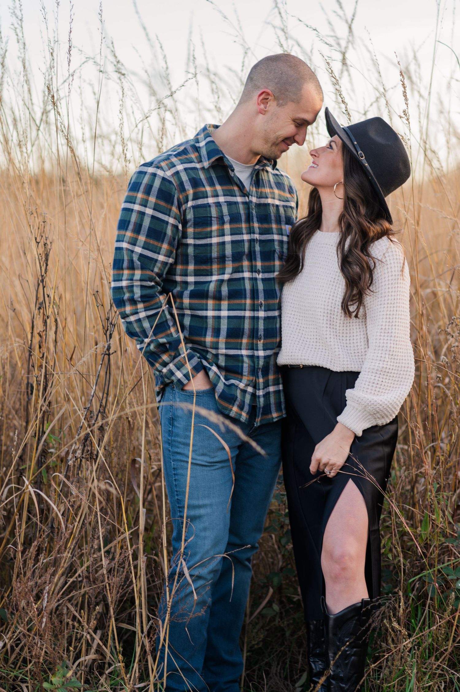 A couple embraces tenderly while standing in tall grass during golden hour.