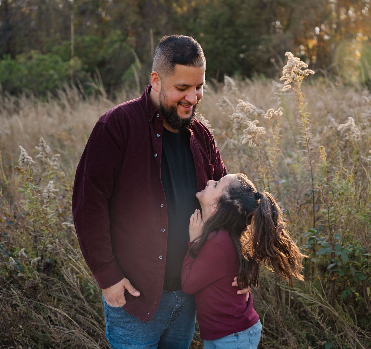 Family sharing candid moments together in tall grass during golden hour sunset.