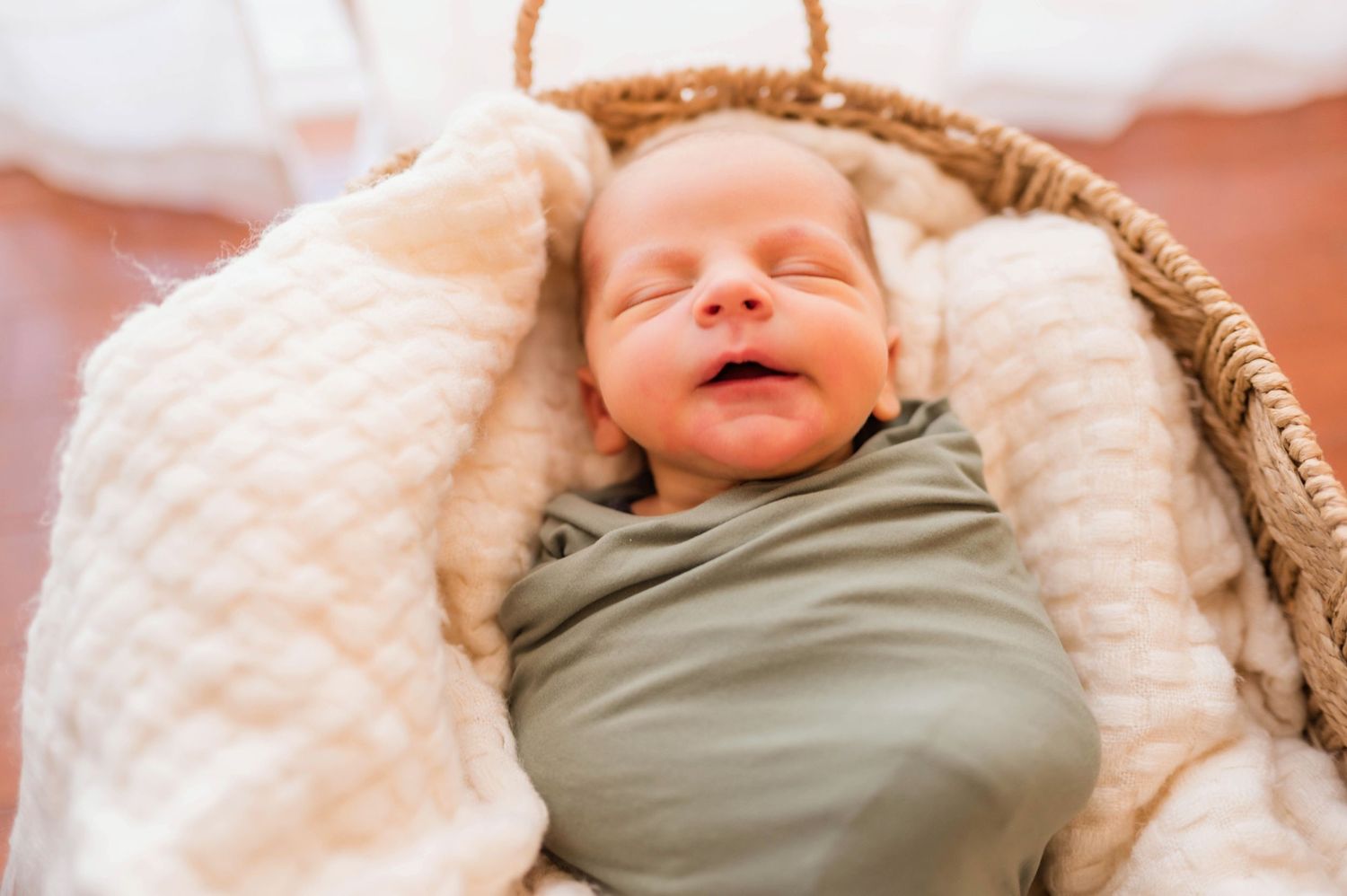 Sleeping newborn wrapped in olive green swaddle on cream textured blanket.
