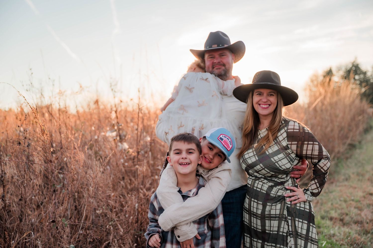 Family wearing western attire poses together in a natural outdoor setting.