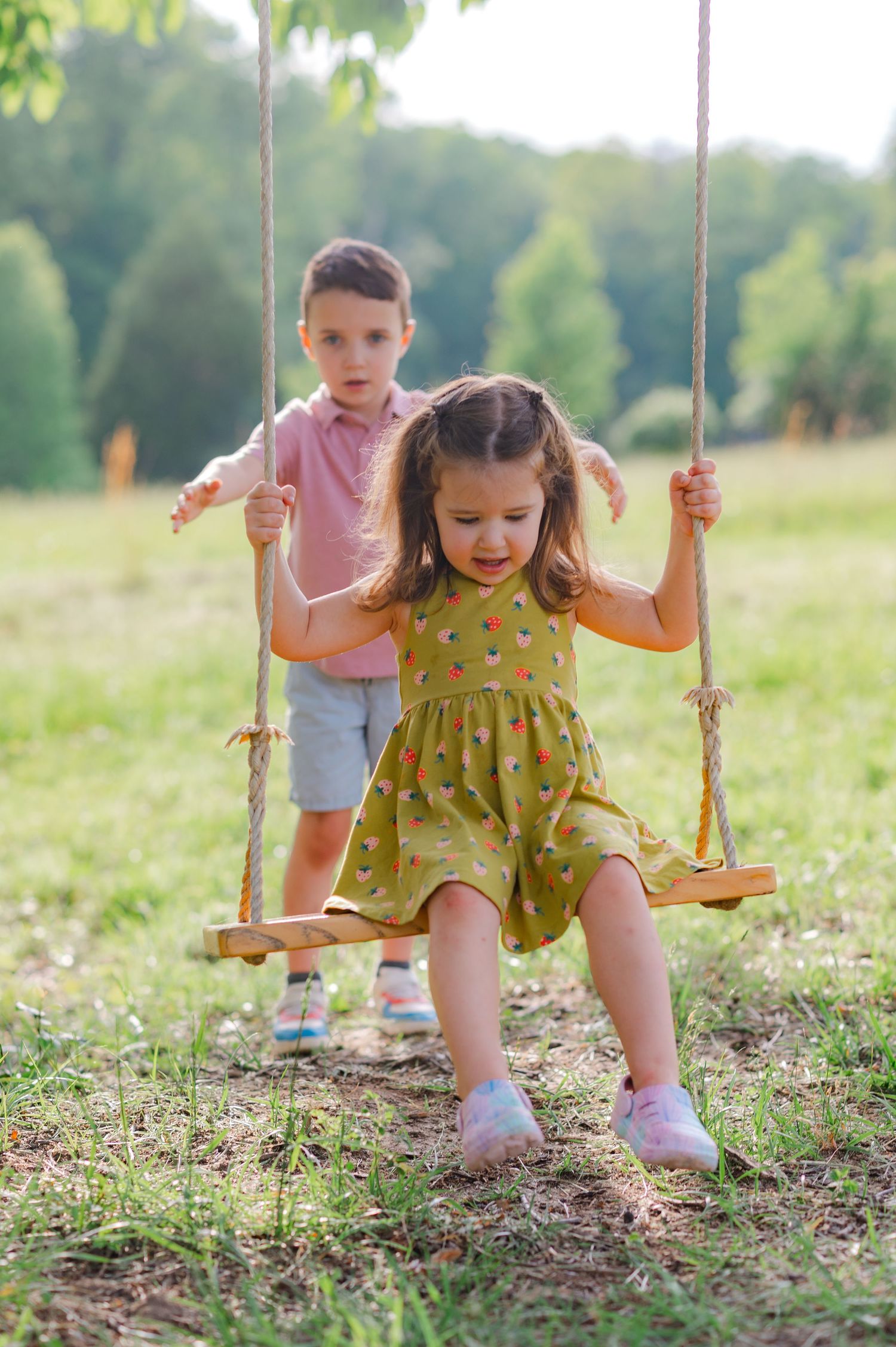 Child playing on wooden swing set in sunny meadow during summer.