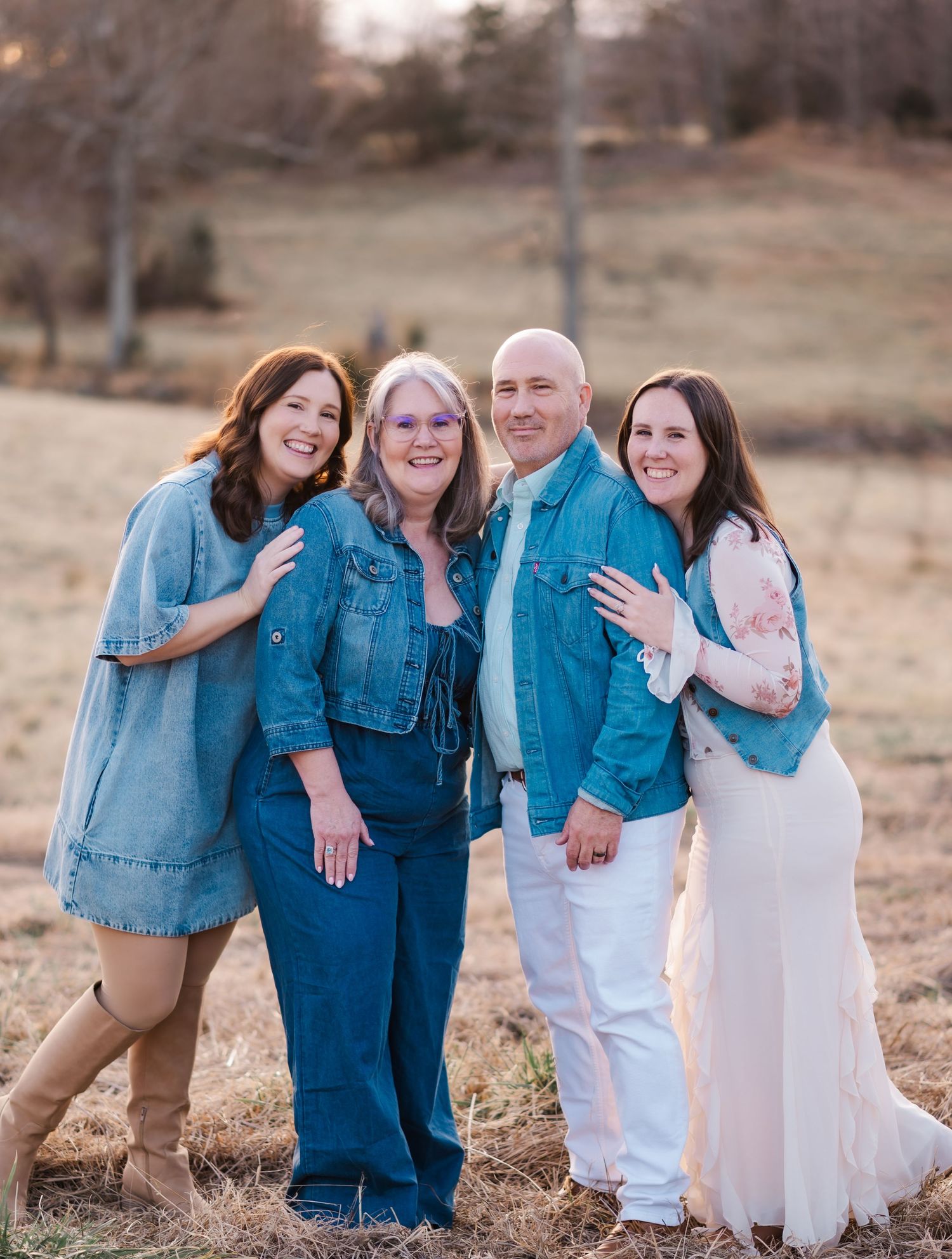 A group in coordinated denim and white outfits poses together in a rustic outdoor setting during golden hour.