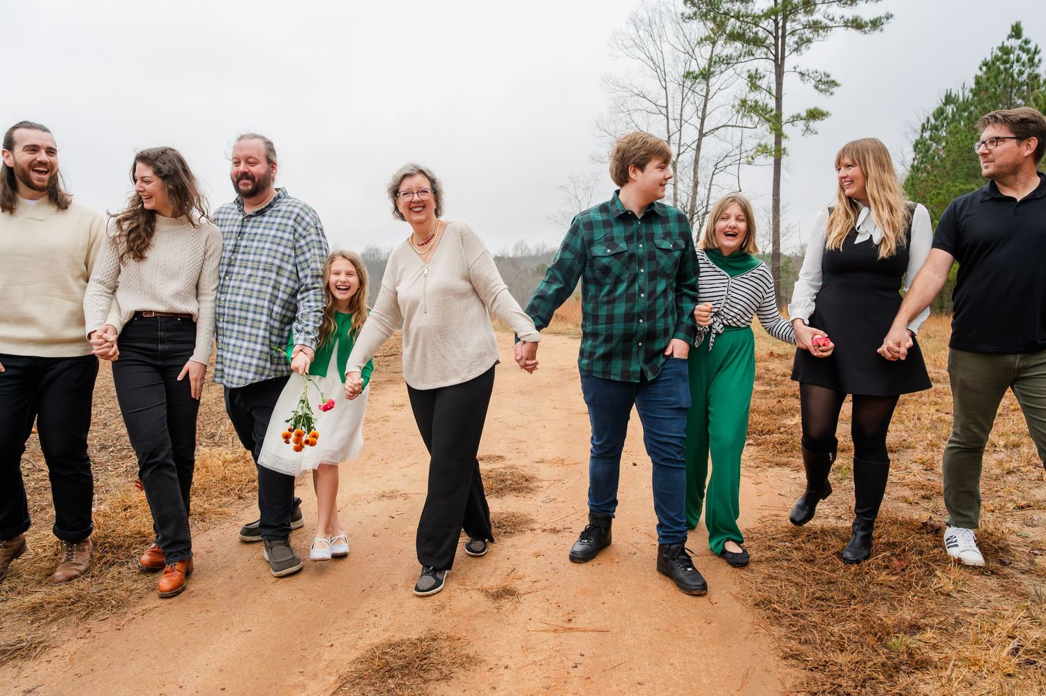 Group of people walking and laughing together on a dirt path through pine trees.