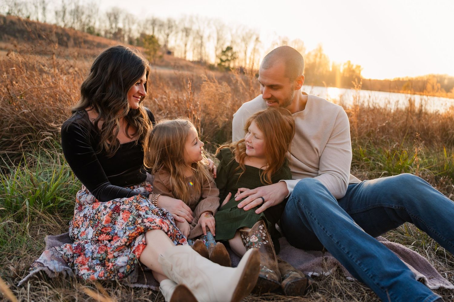 A family sitting together on grass during sunset with golden light filtering through trees.