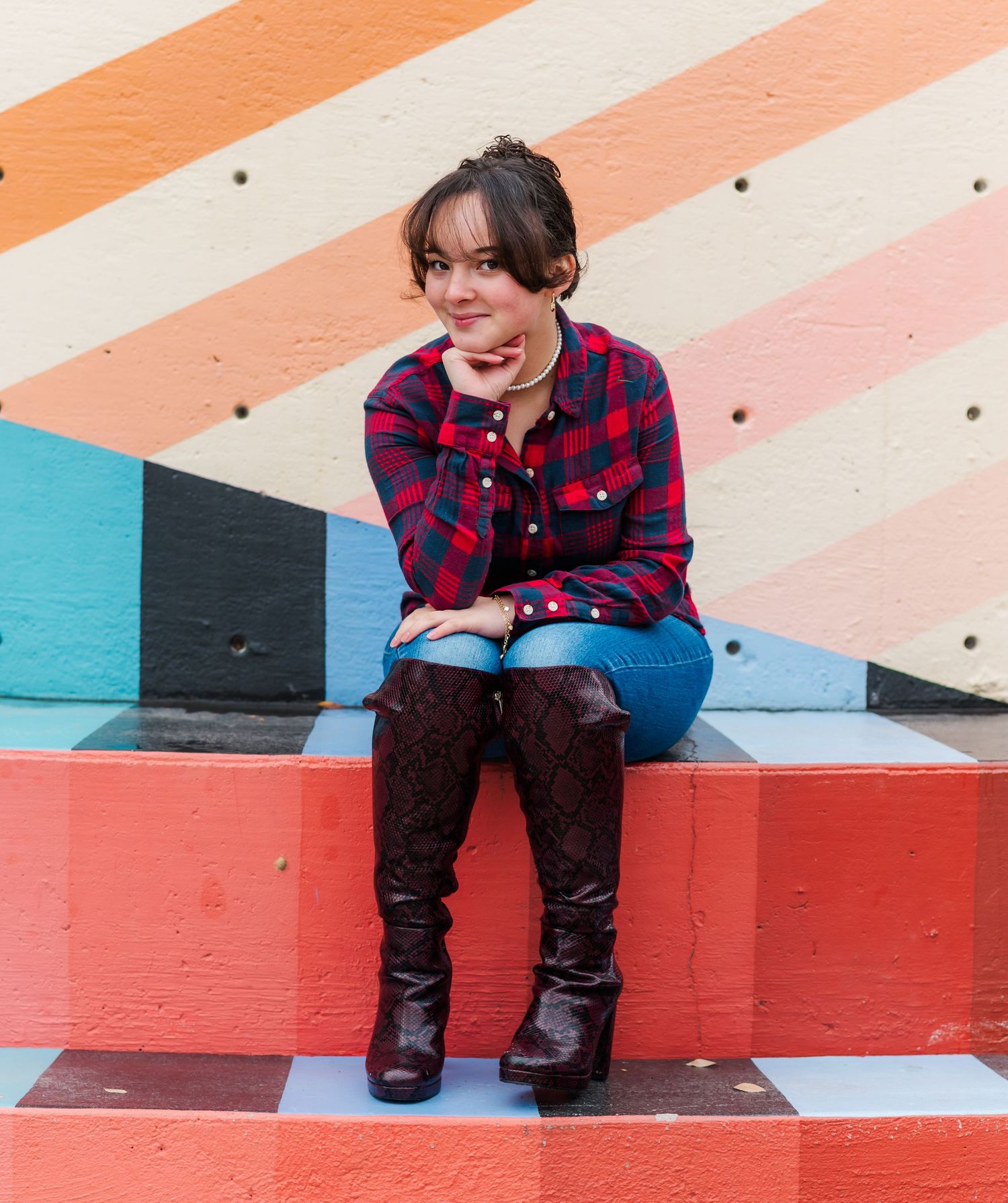 Person in plaid shirt and boots sits on colorful striped wall bench with joyful expression.