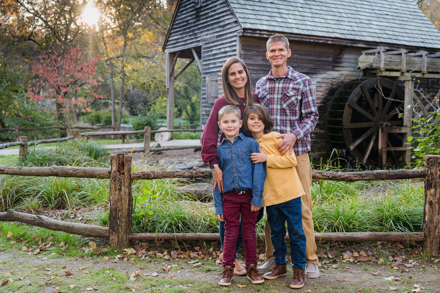 Rustic outdoor family photo session at historic log cabin with wooden fence in autumn.