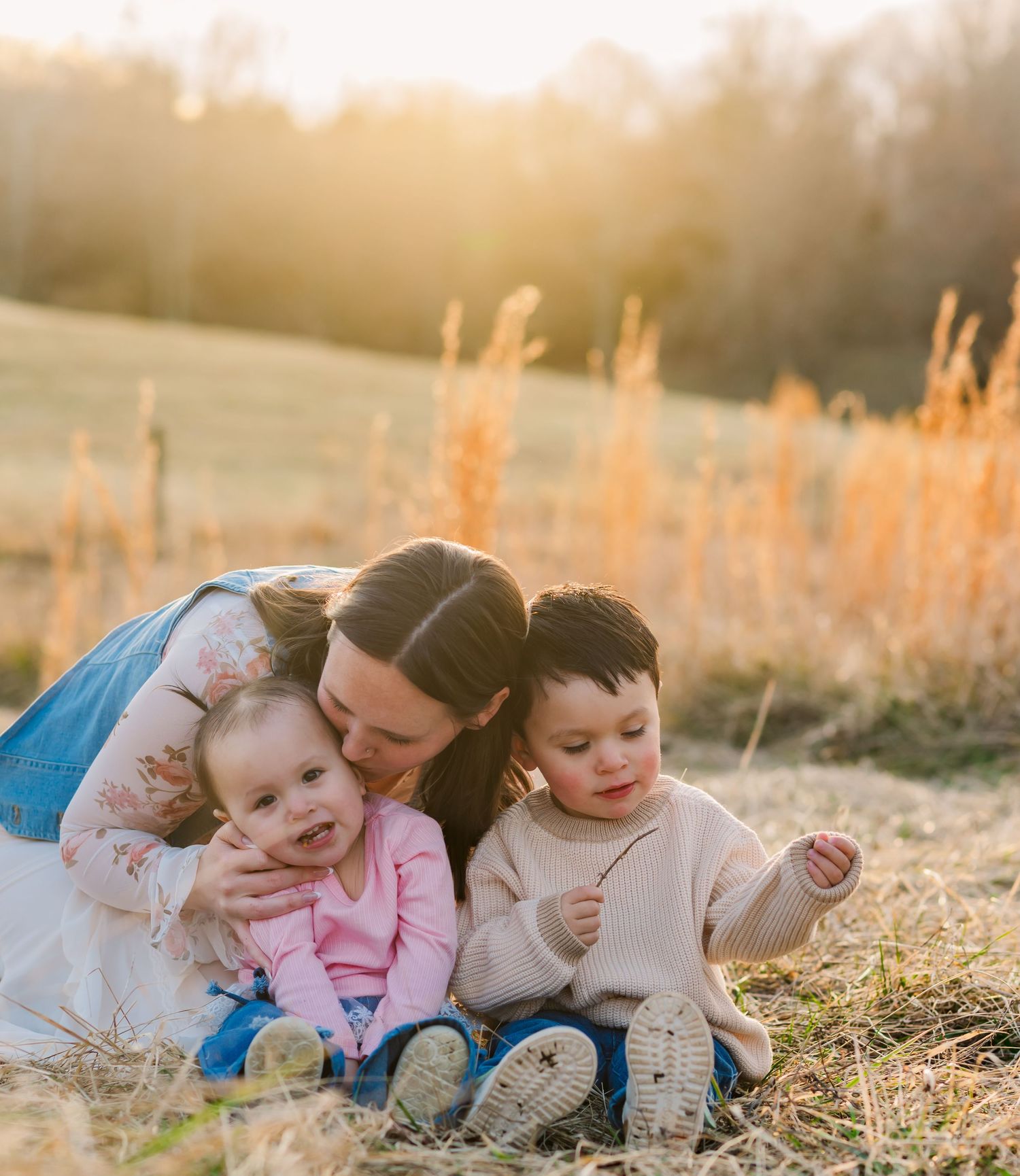Candid family moments captured while laying in tall grass during golden hour photography session.