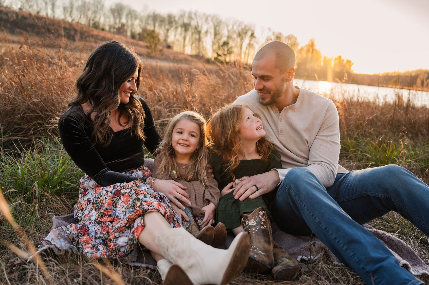 Family enjoying a warm sunset moment together on a blanket in a grassy field during golden hour.