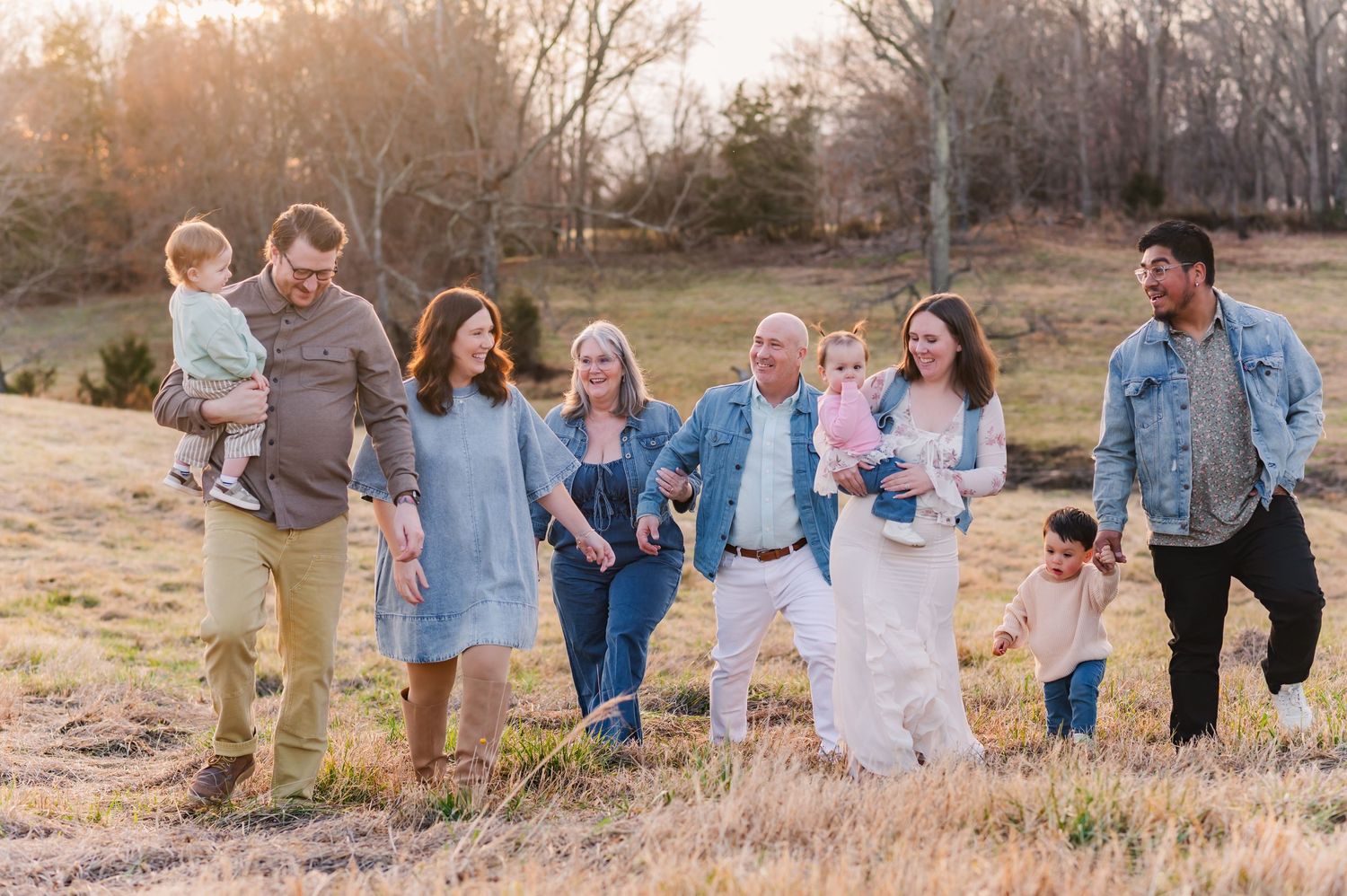 Family members walk together through a golden field at sunset wearing coordinated blue and white outfits.
