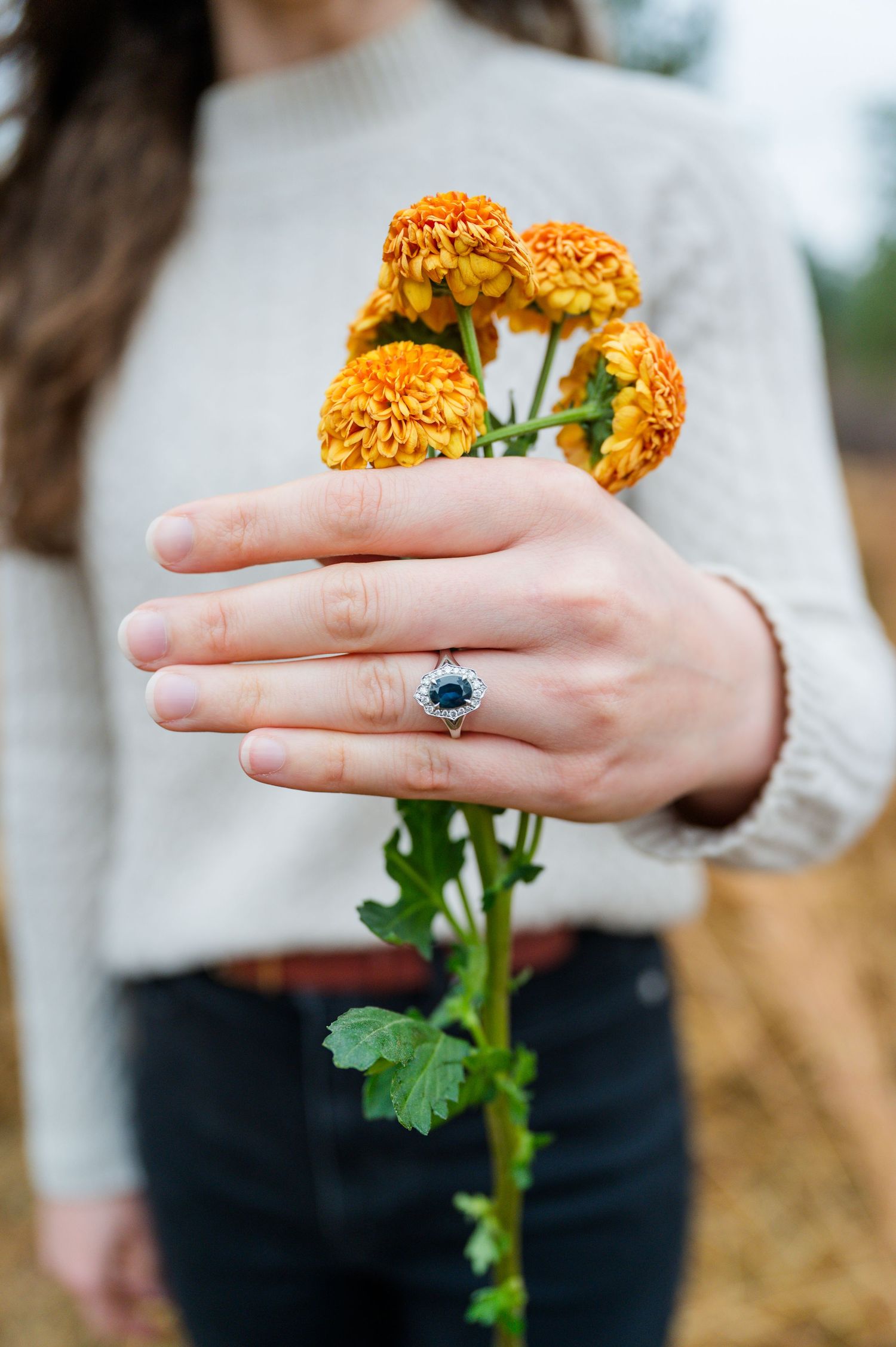 Close-up of hand holding orange marigold flower with sapphire ring.