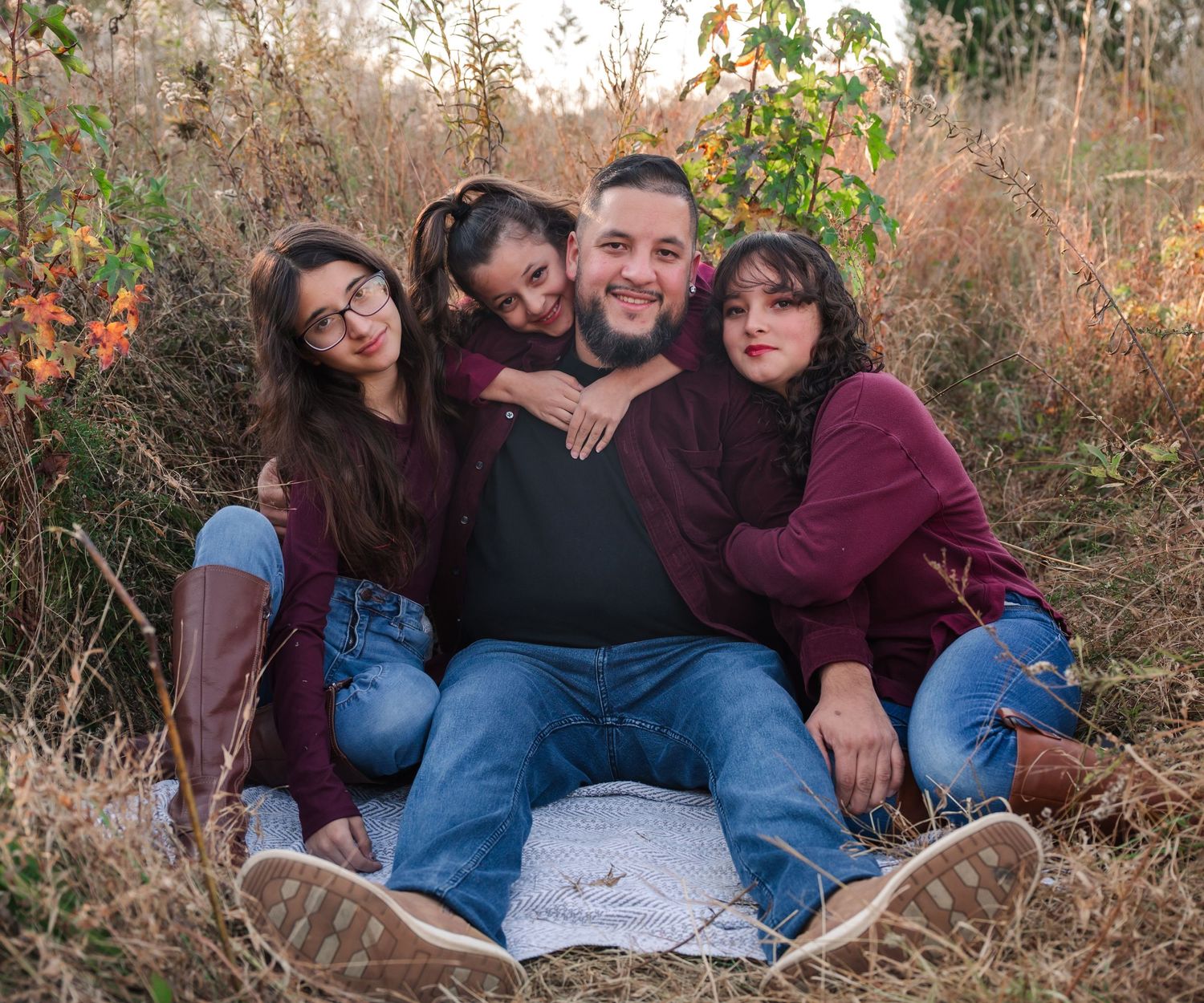 Family relaxing together on blanket surrounded by autumn foliage during outdoor photo session.