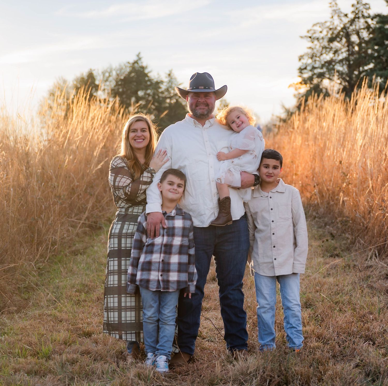 Family portrait session at golden hour with tall grass and warm sunset lighting.