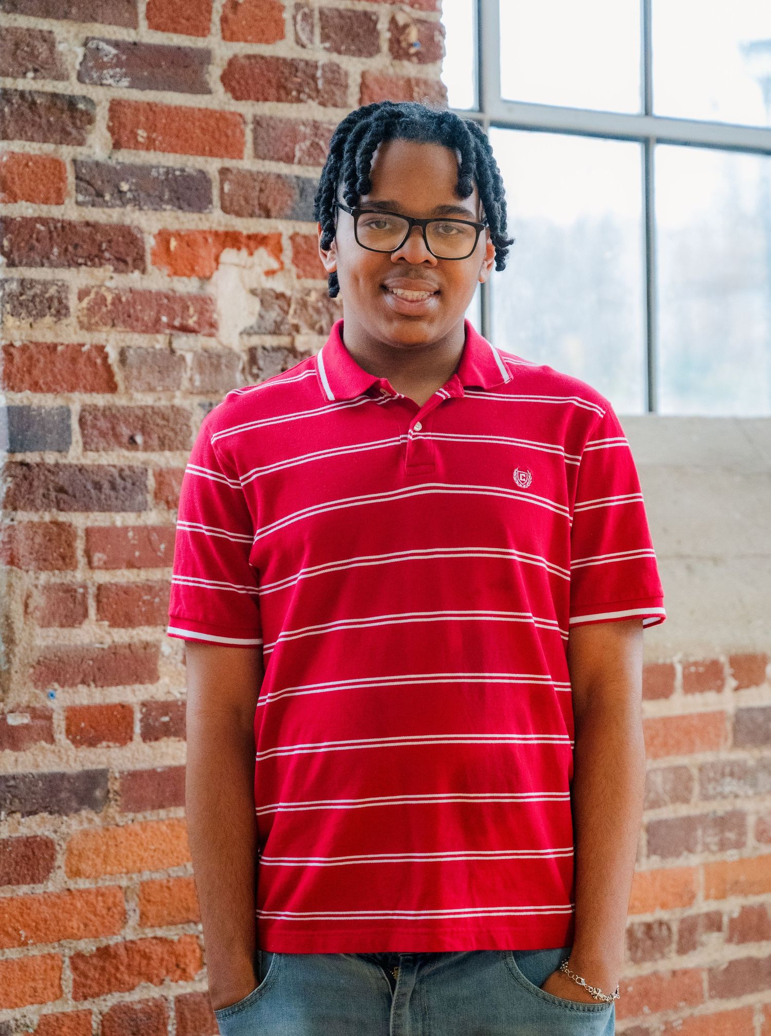 Person wearing a red striped polo shirt stands against a brick wall background.