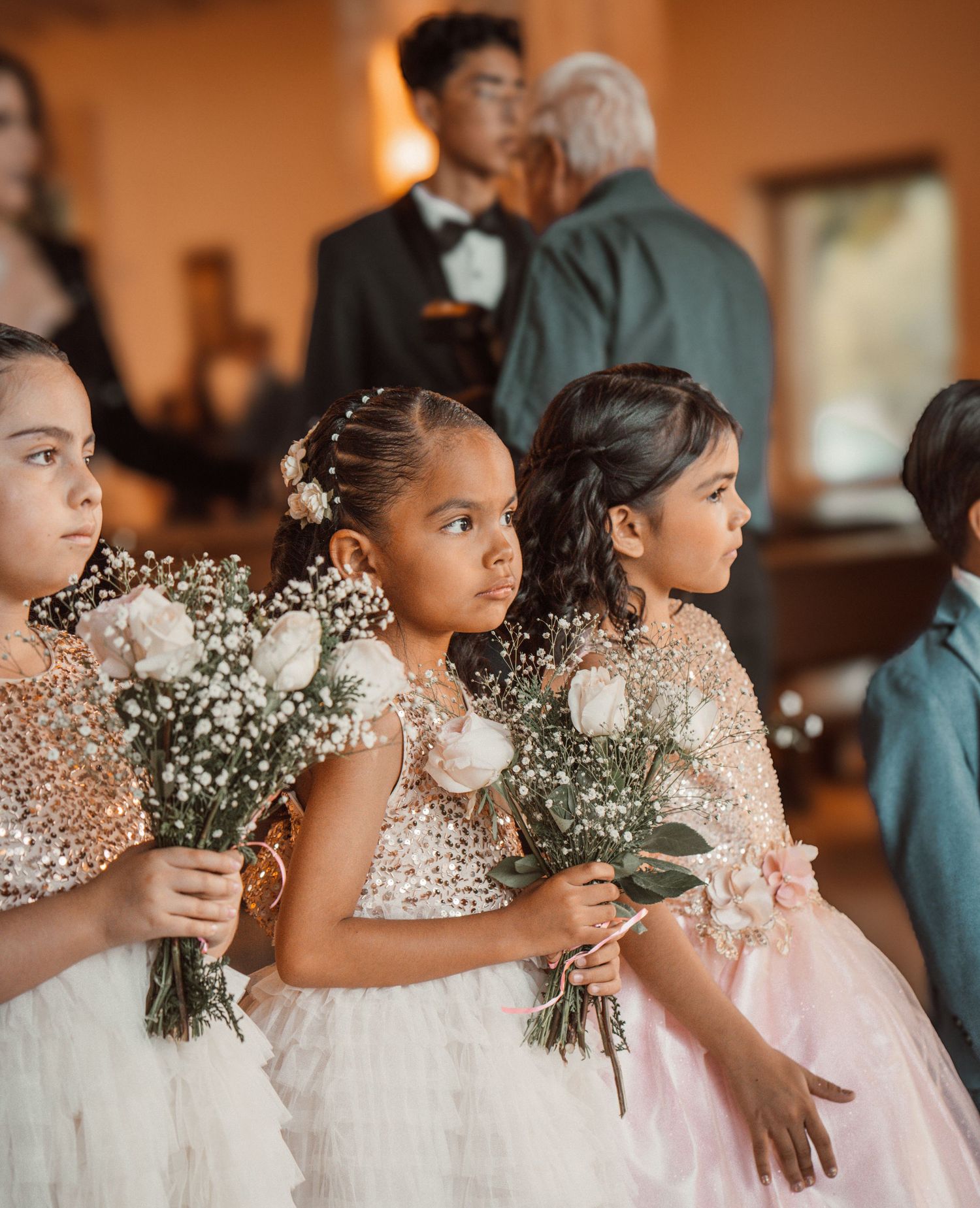 Young bridesmaids in pink dresses holding baby's breath bouquets stand in line at a wedding ceremony.