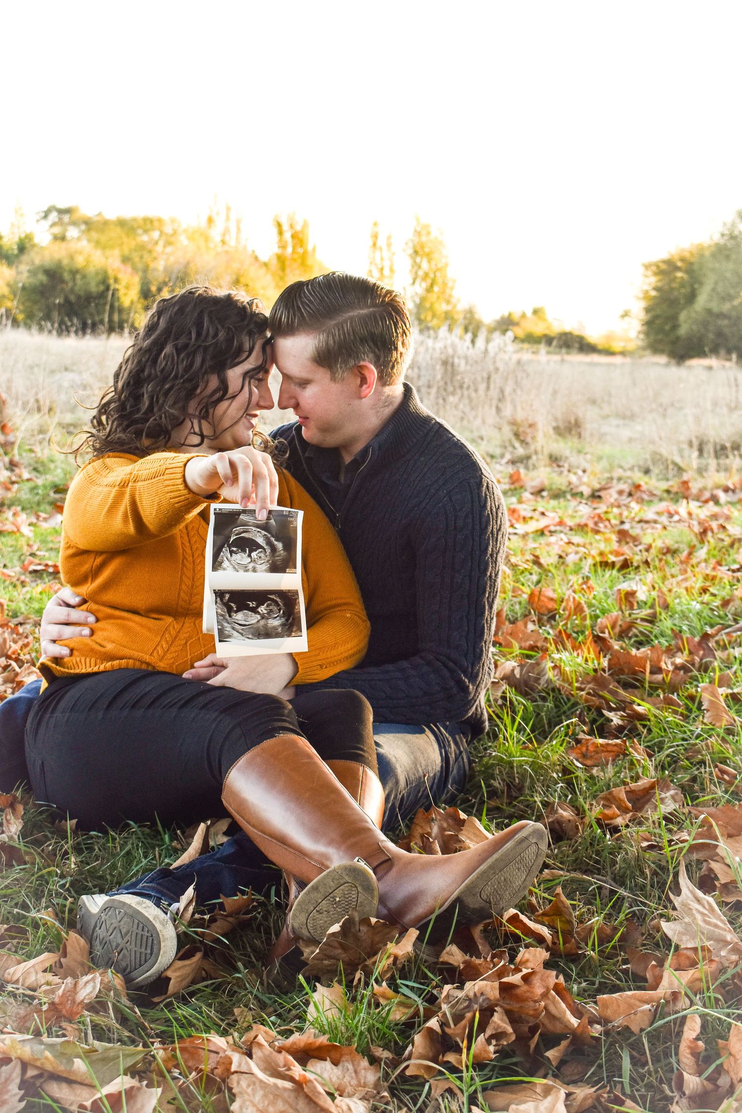 Pregnancy announcement photoshoot with ultrasound picture in fall setting.
